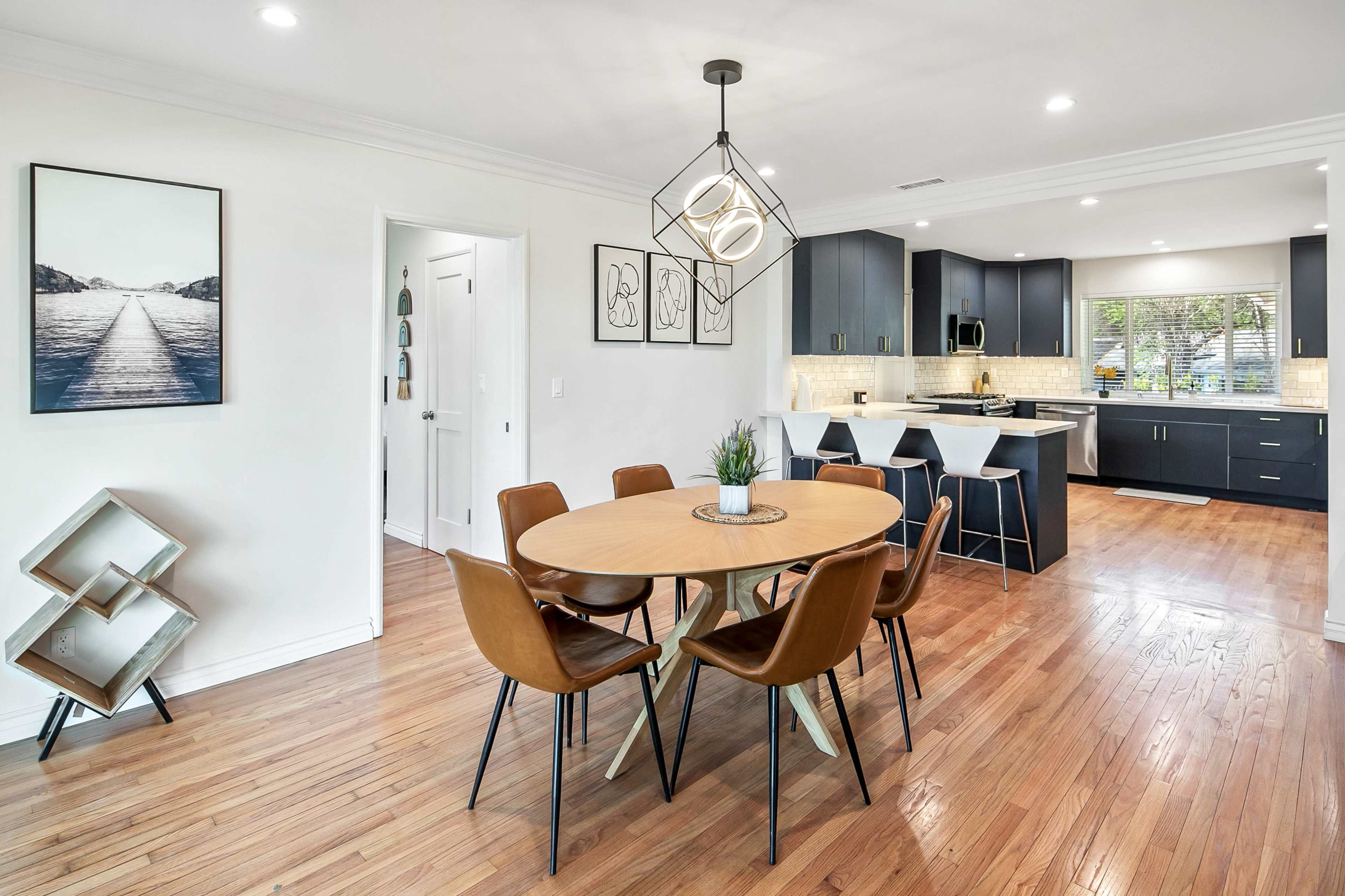 A modern dining area features a round table surrounded by four brown chairs, with a view into a kitchen that has navy blue cabinets and white countertops.