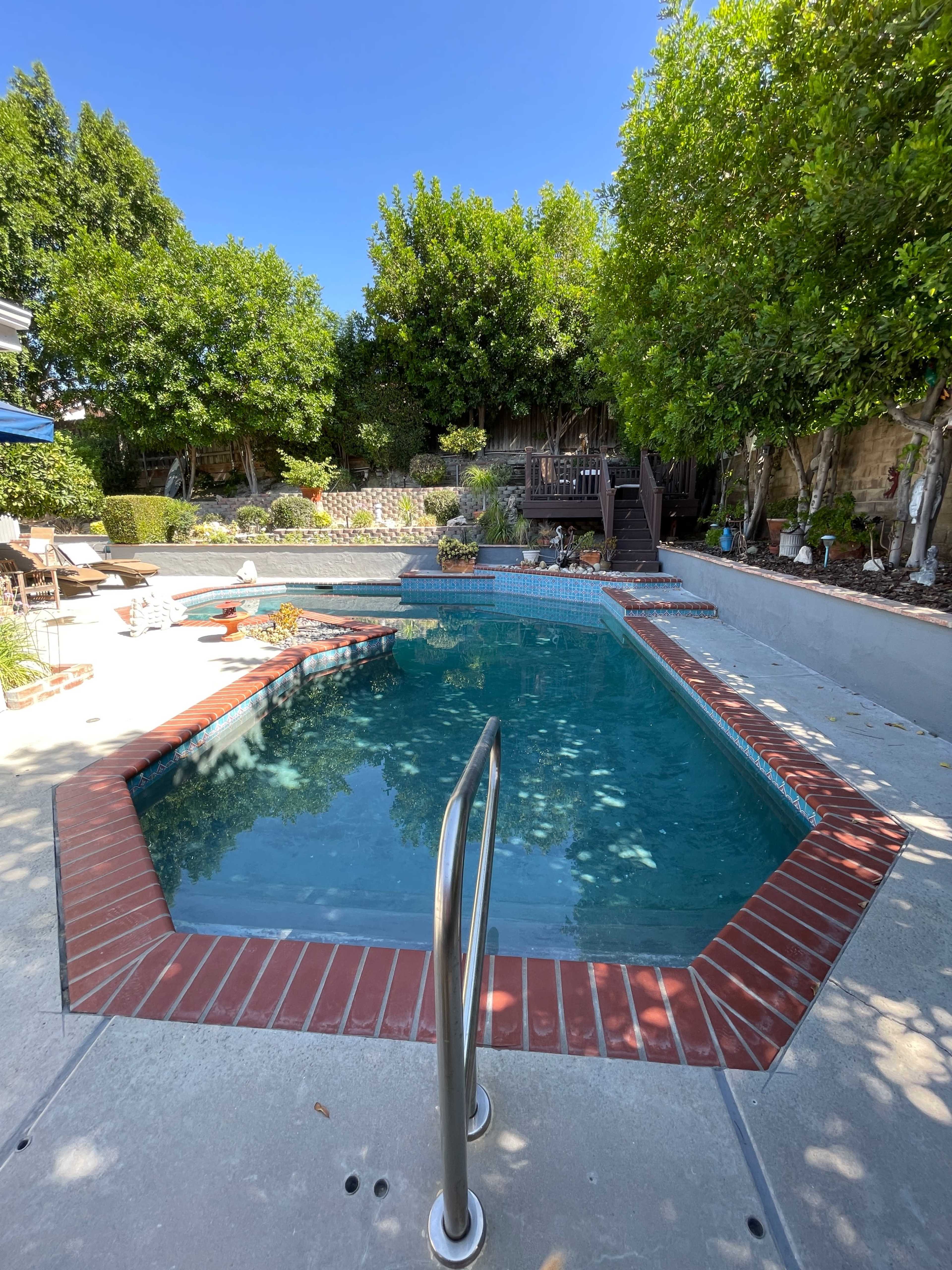 An octagonal swimming pool surrounded by a landscaped garden and patio area with wooden steps leading to an elevated deck.