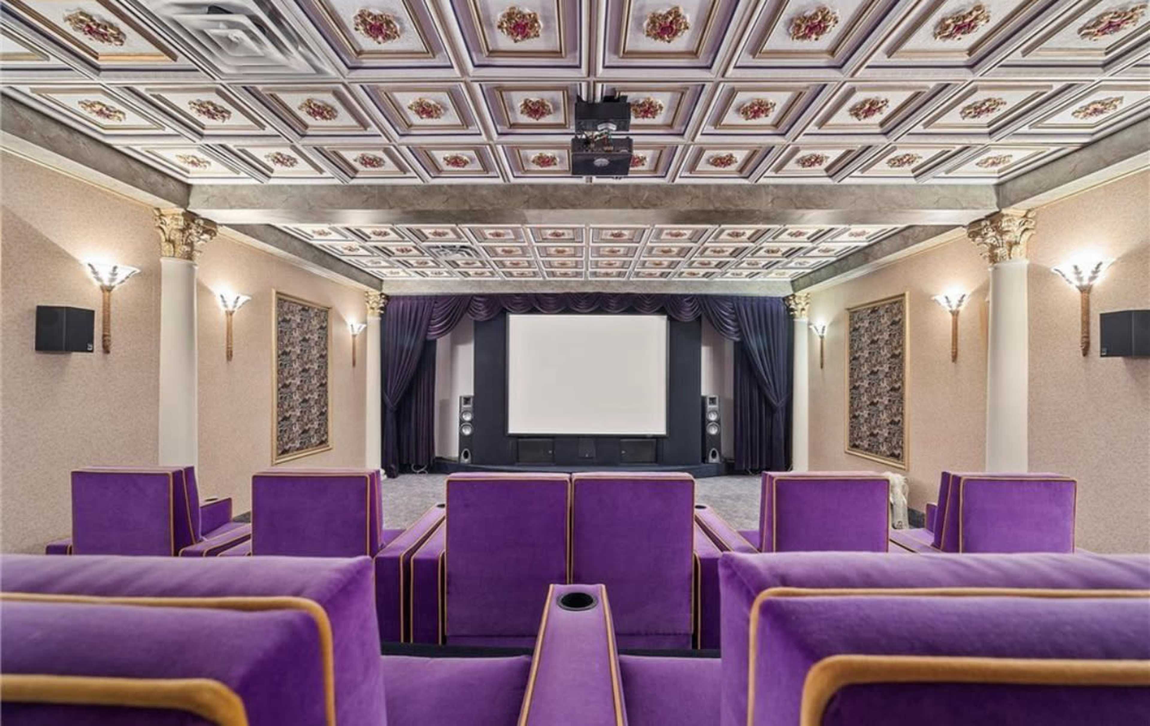 A home theater with purple seating, a large screen, and a decorative ceiling with ornate designs.