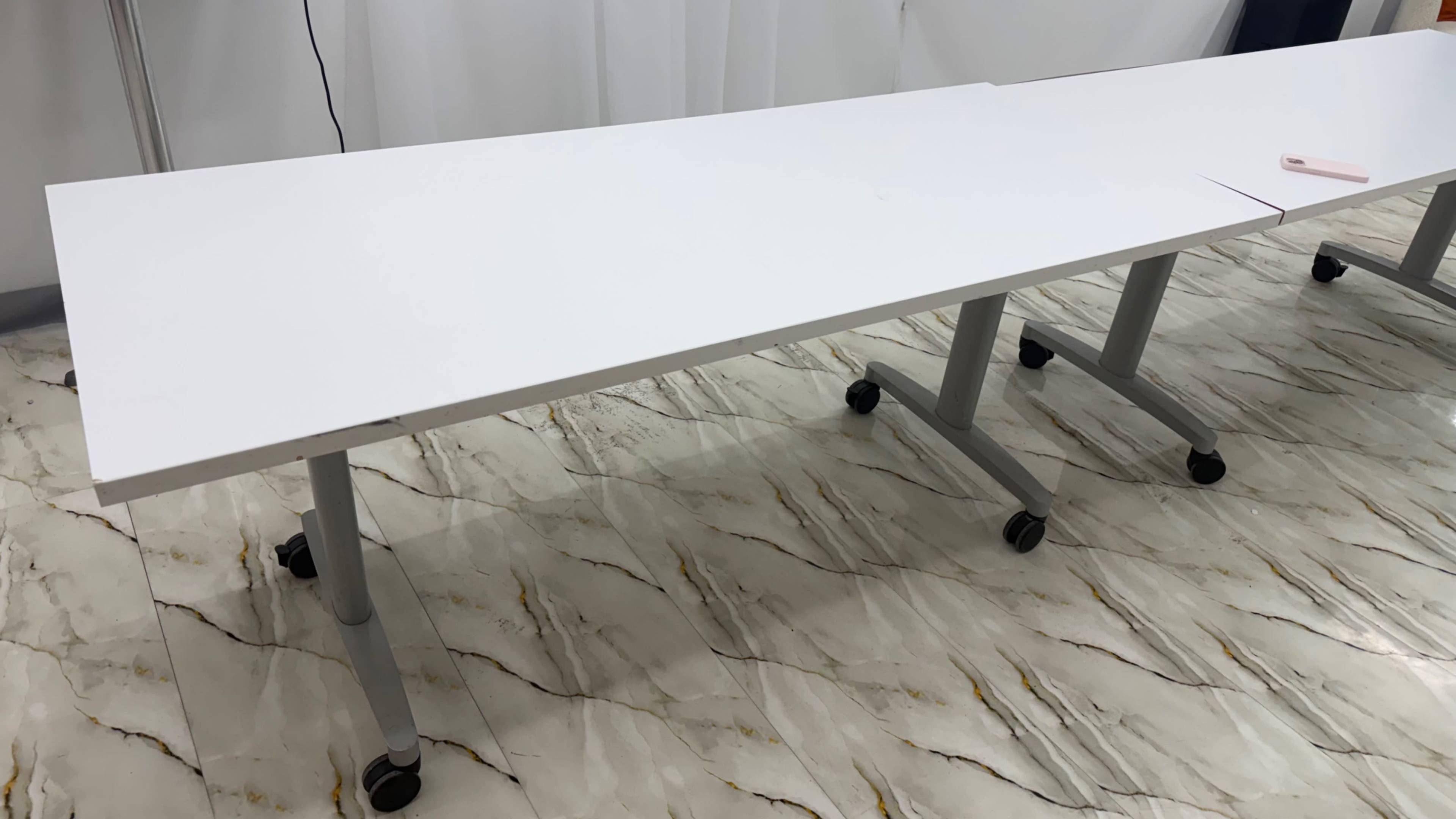 The image shows a long, white table on wheels positioned on a marble-patterned floor.
