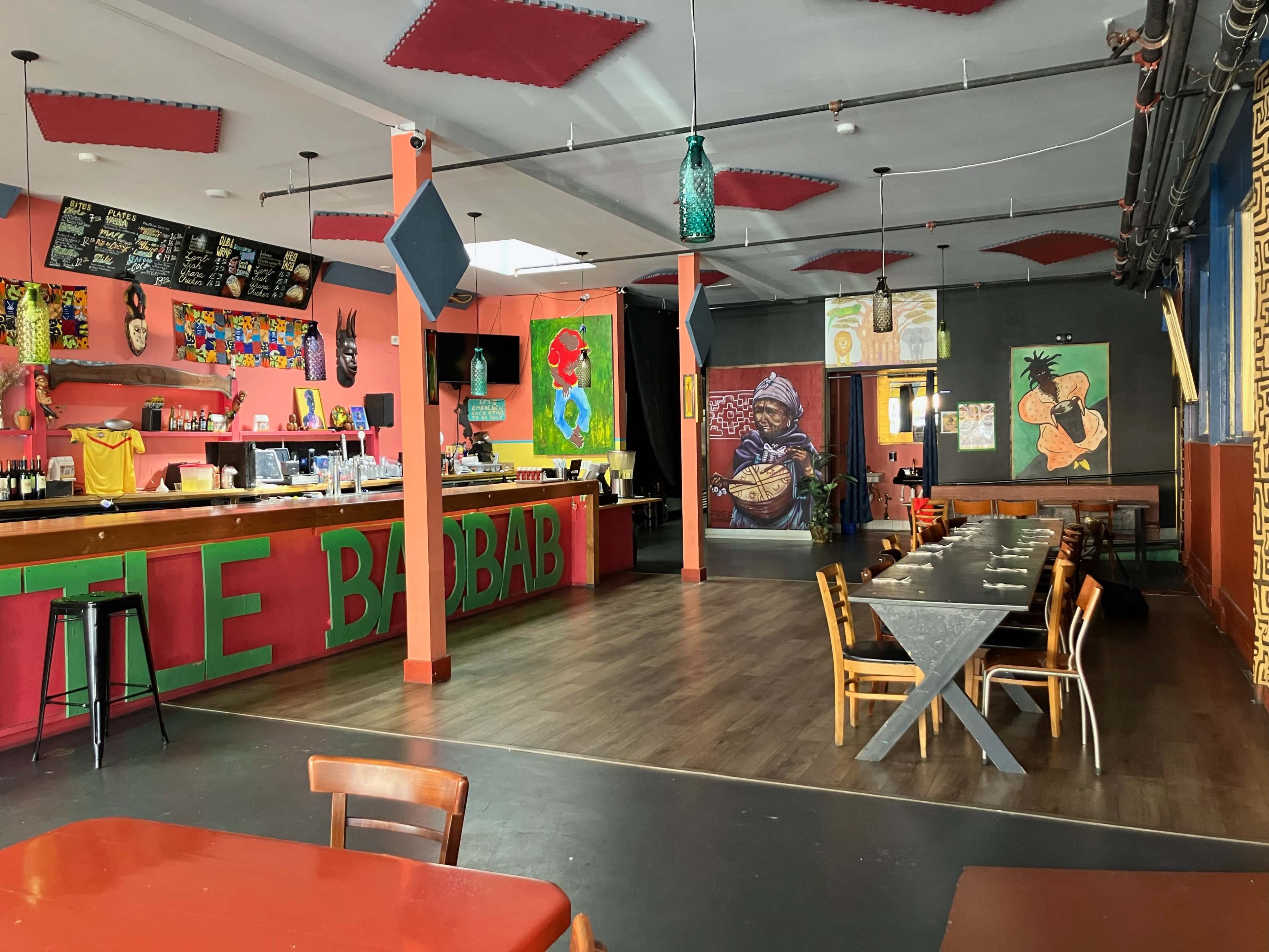 A colorful restaurant interior with a bar, decorated walls featuring artwork, and tables set for dining.