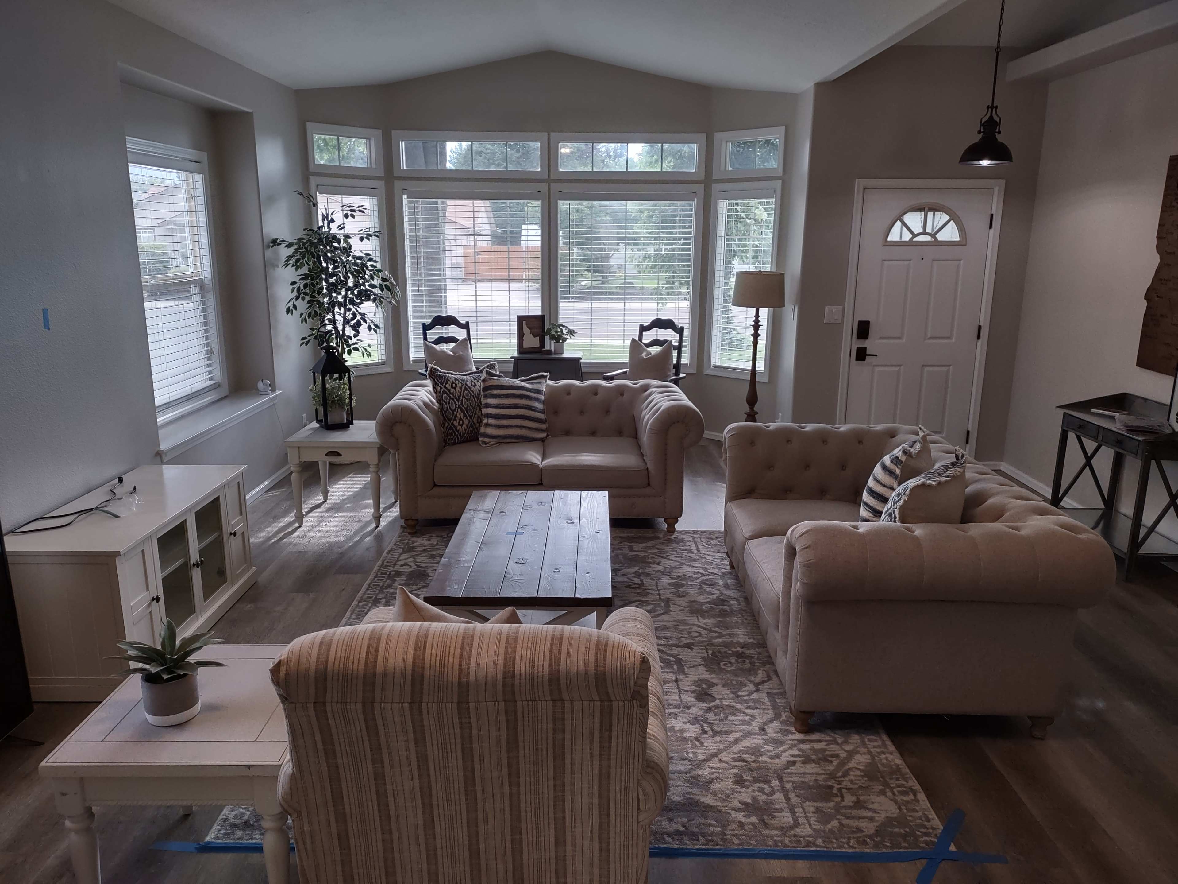 A living room with two beige couches facing a coffee table, surrounded by large windows and a front door.