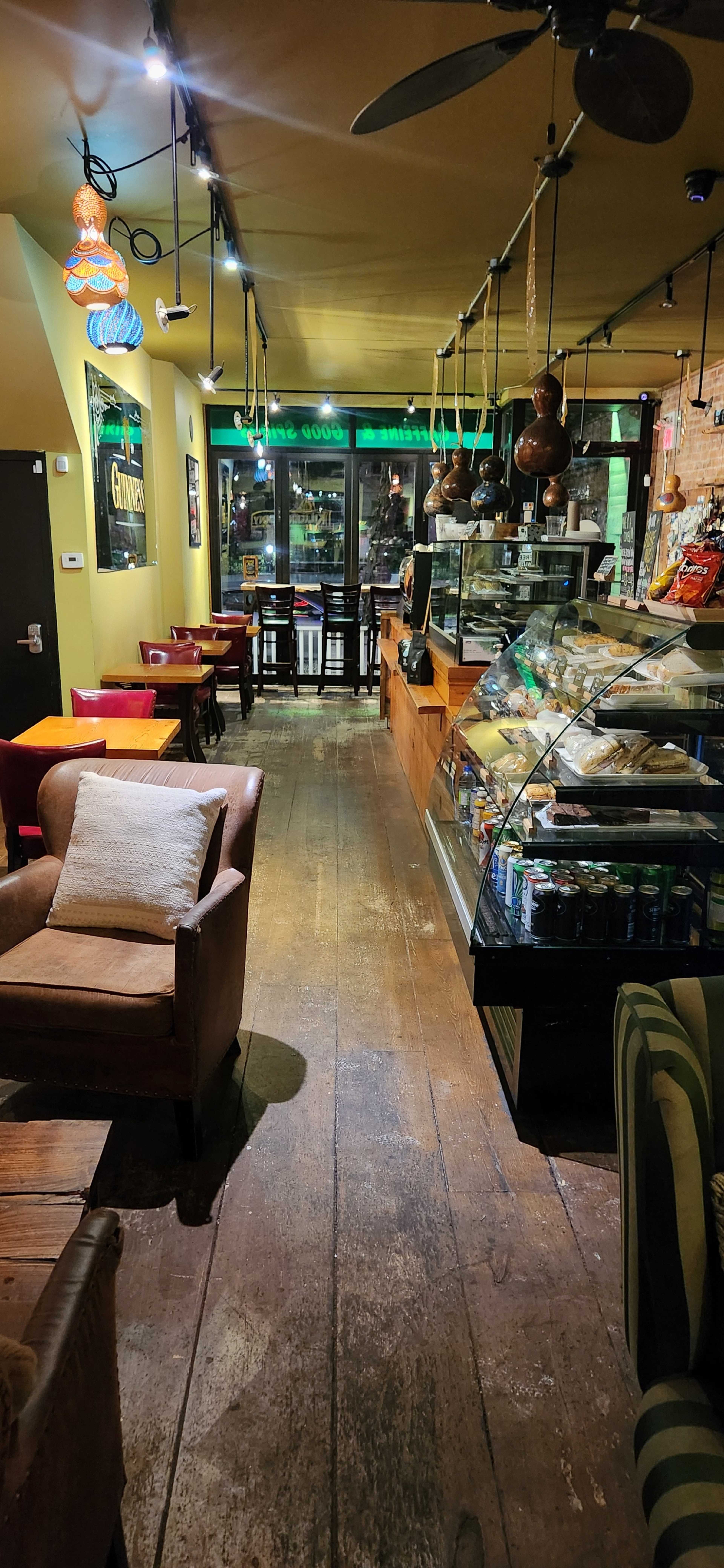 The image shows a cozy café interior featuring wooden floors, a display case filled with snacks, and seating areas with colorful chairs.