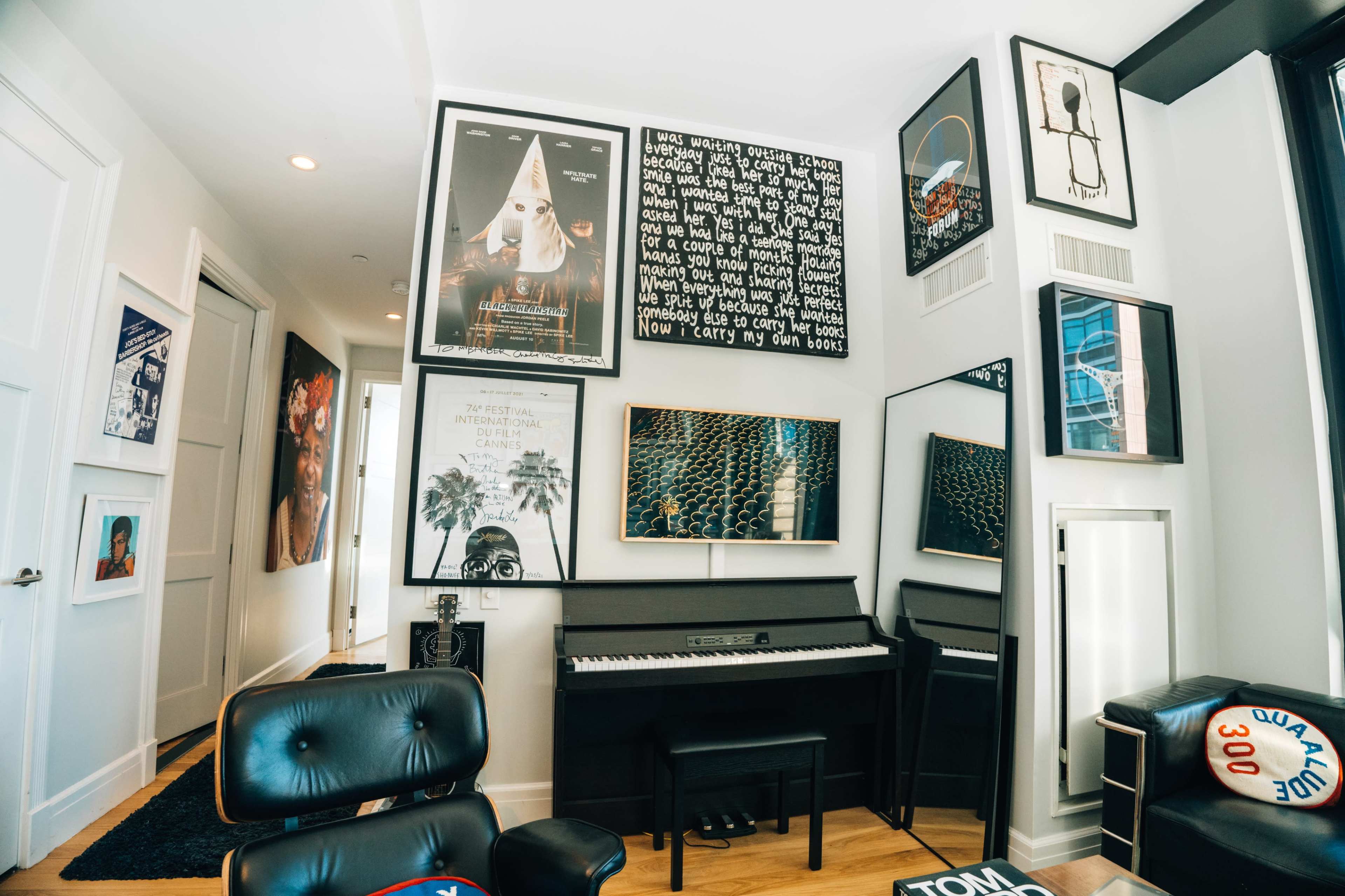 A modern room features a black piano against a wall adorned with various framed artworks and photographs.