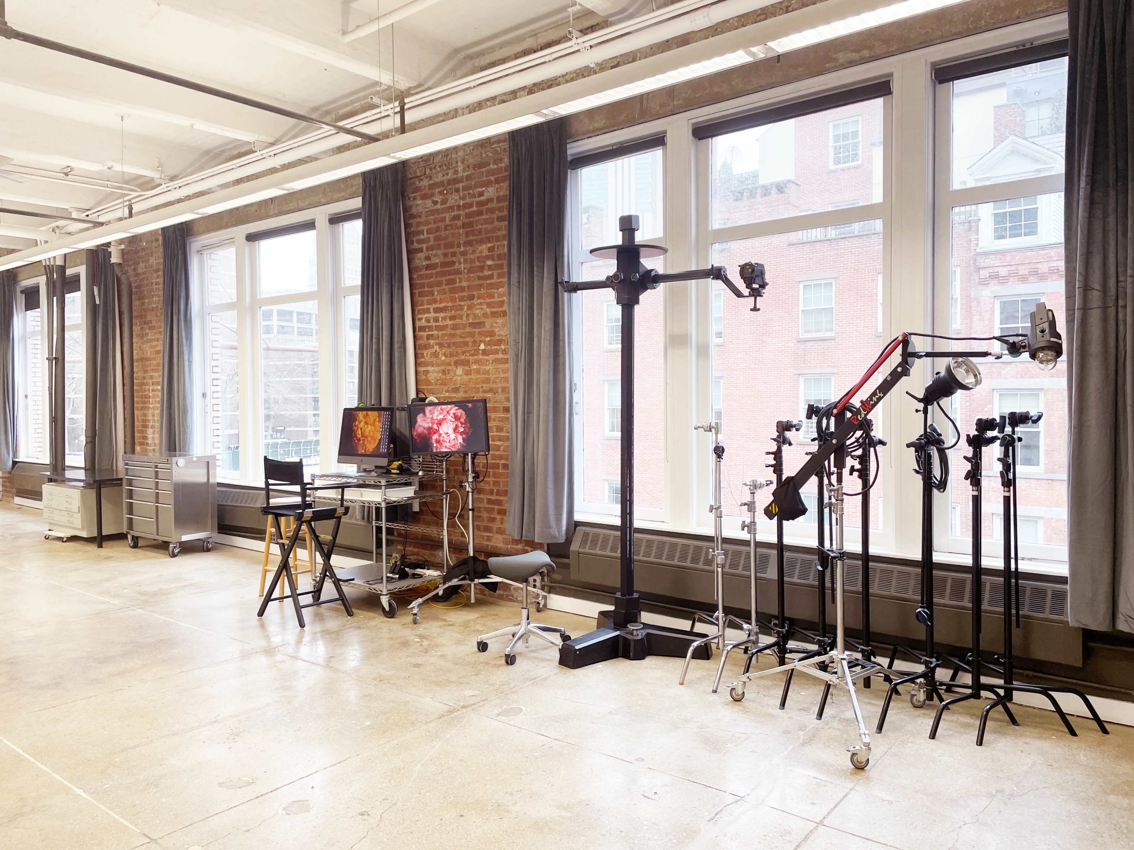 The image displays a spacious room with large windows, featuring various lab equipment, including monitors, a rolling cart, and several adjustable stands.