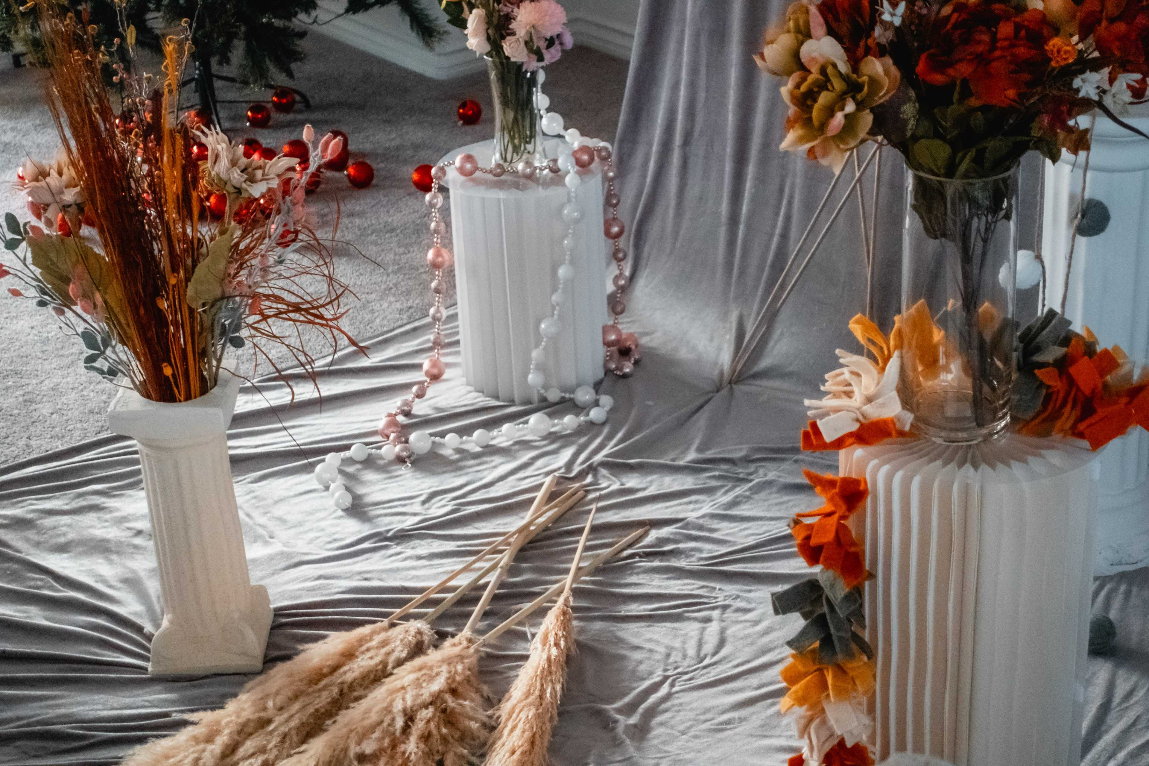 Decorative vases filled with flowers and dried grasses arranged on a gray fabric surface.