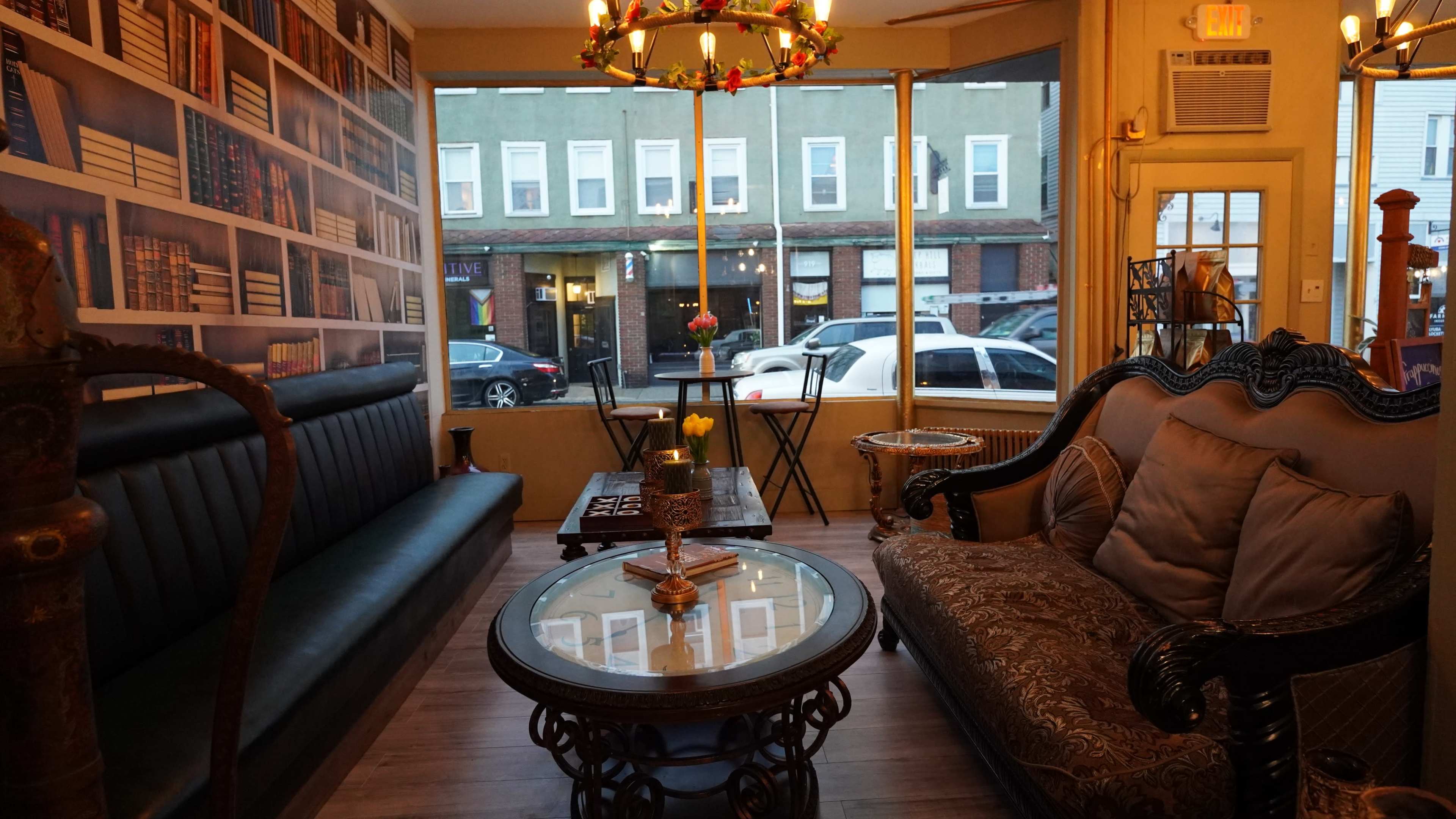 A cozy seating area with two distinct sofas facing a glass coffee table, set against a backdrop of a bookshelf mural and large windows revealing a street view outside.