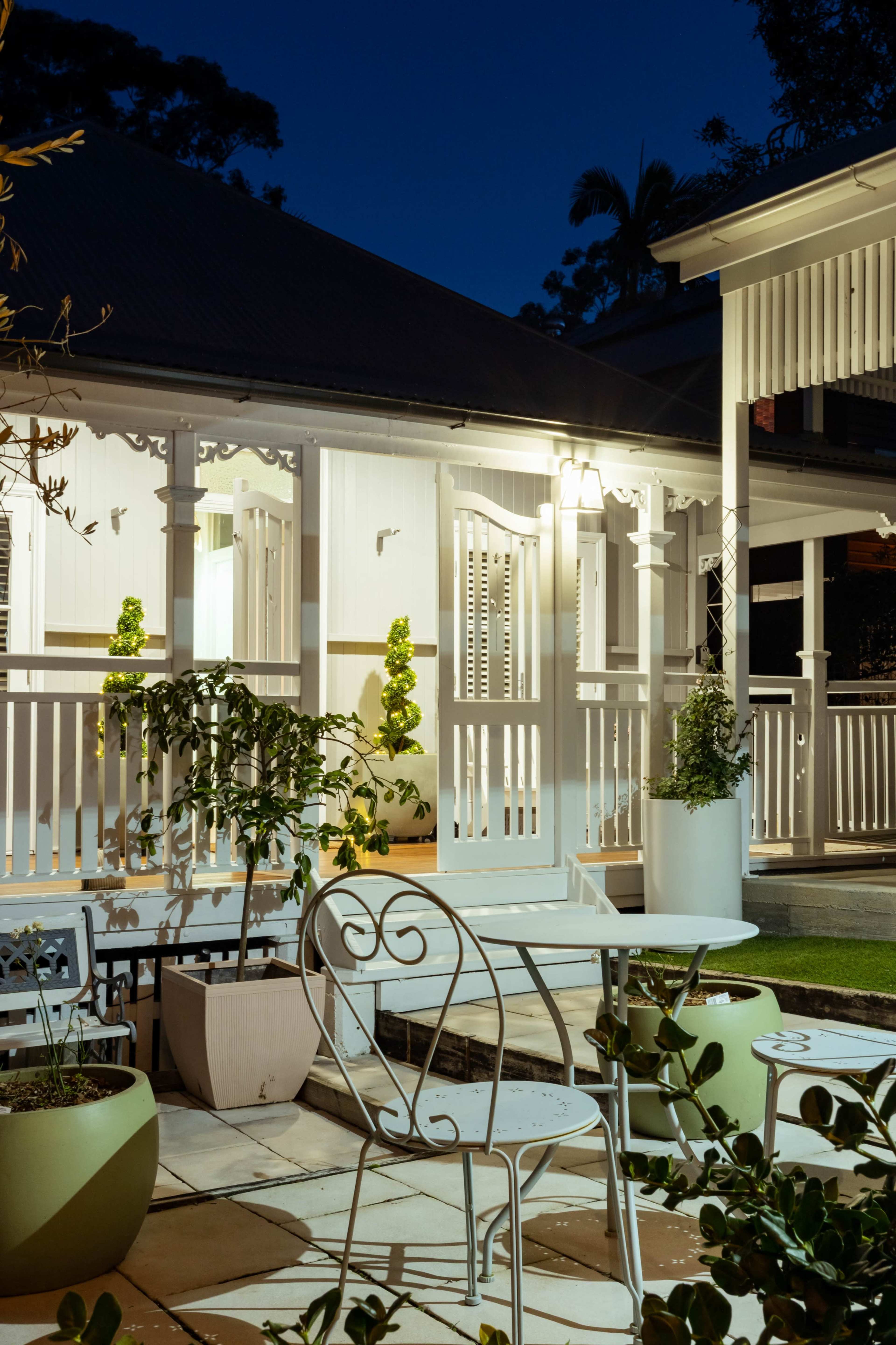 The image shows a well-lit outdoor patio area with white railings and modern furnishings at dusk.