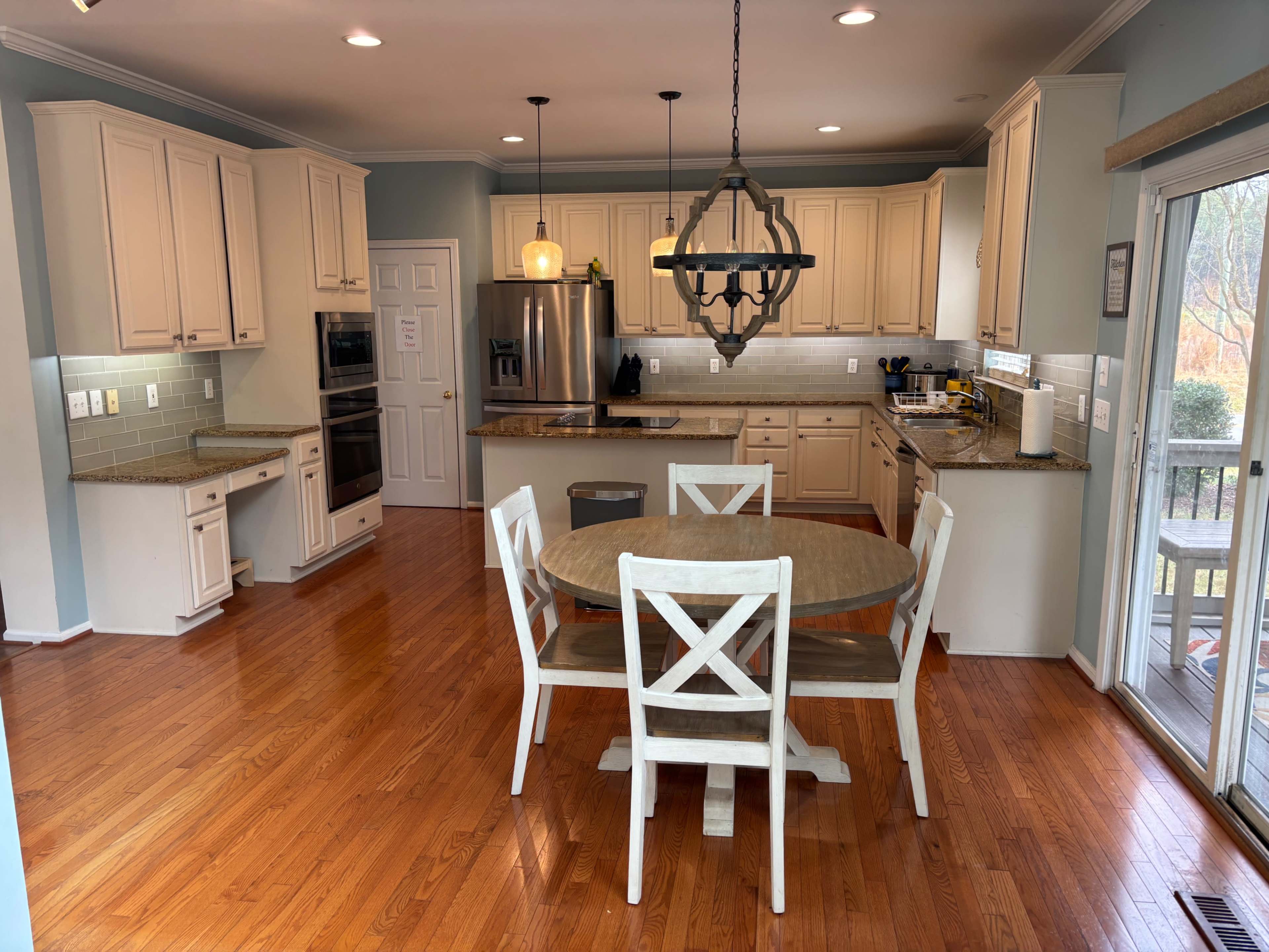 The image depicts a modern kitchen with wooden cabinets, stainless steel appliances, and a round dining table with four chairs.