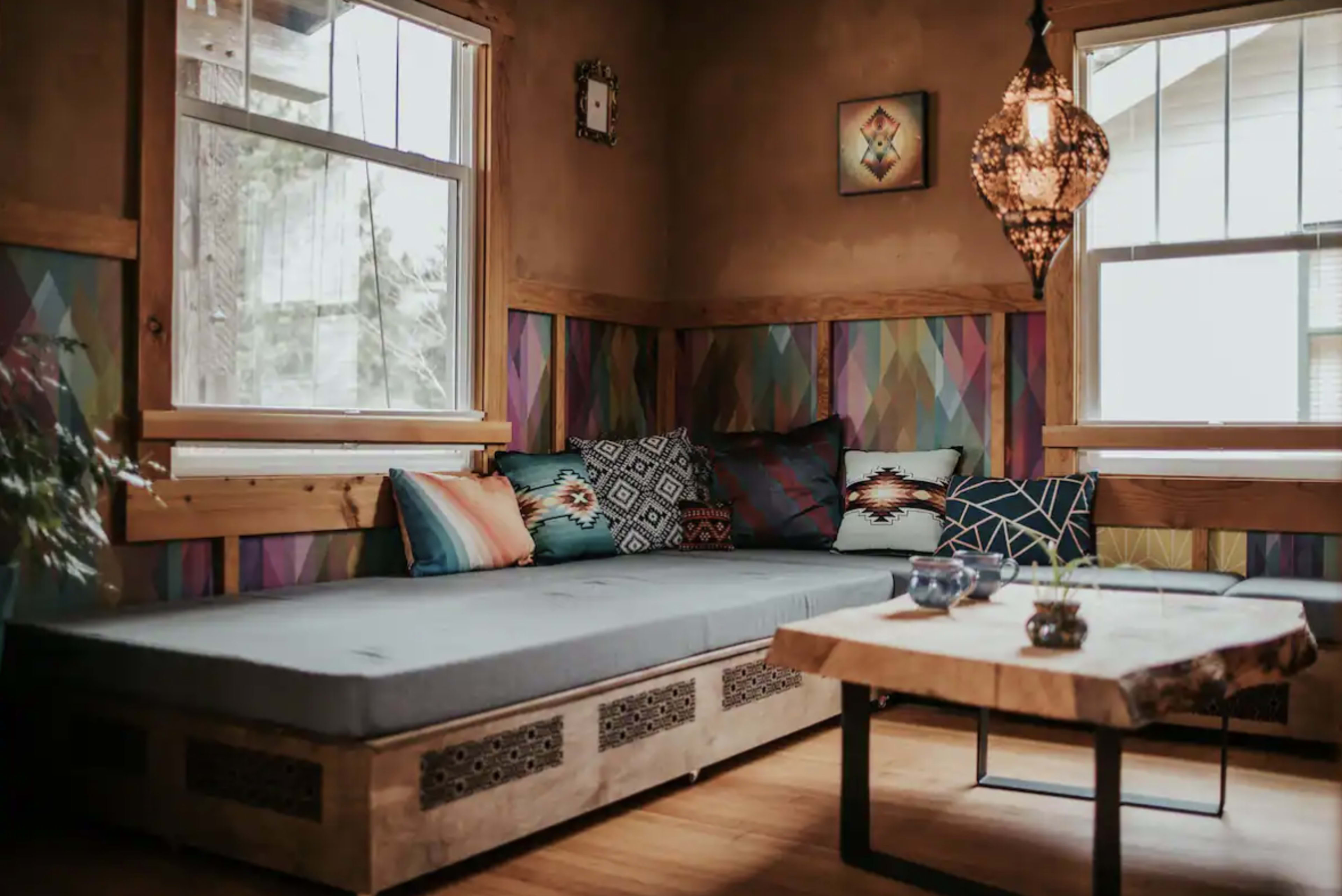 A cozy corner of a room featuring a gray cushioned seating area with decorative pillows, a wooden coffee table, and a pendant light hanging from the ceiling.