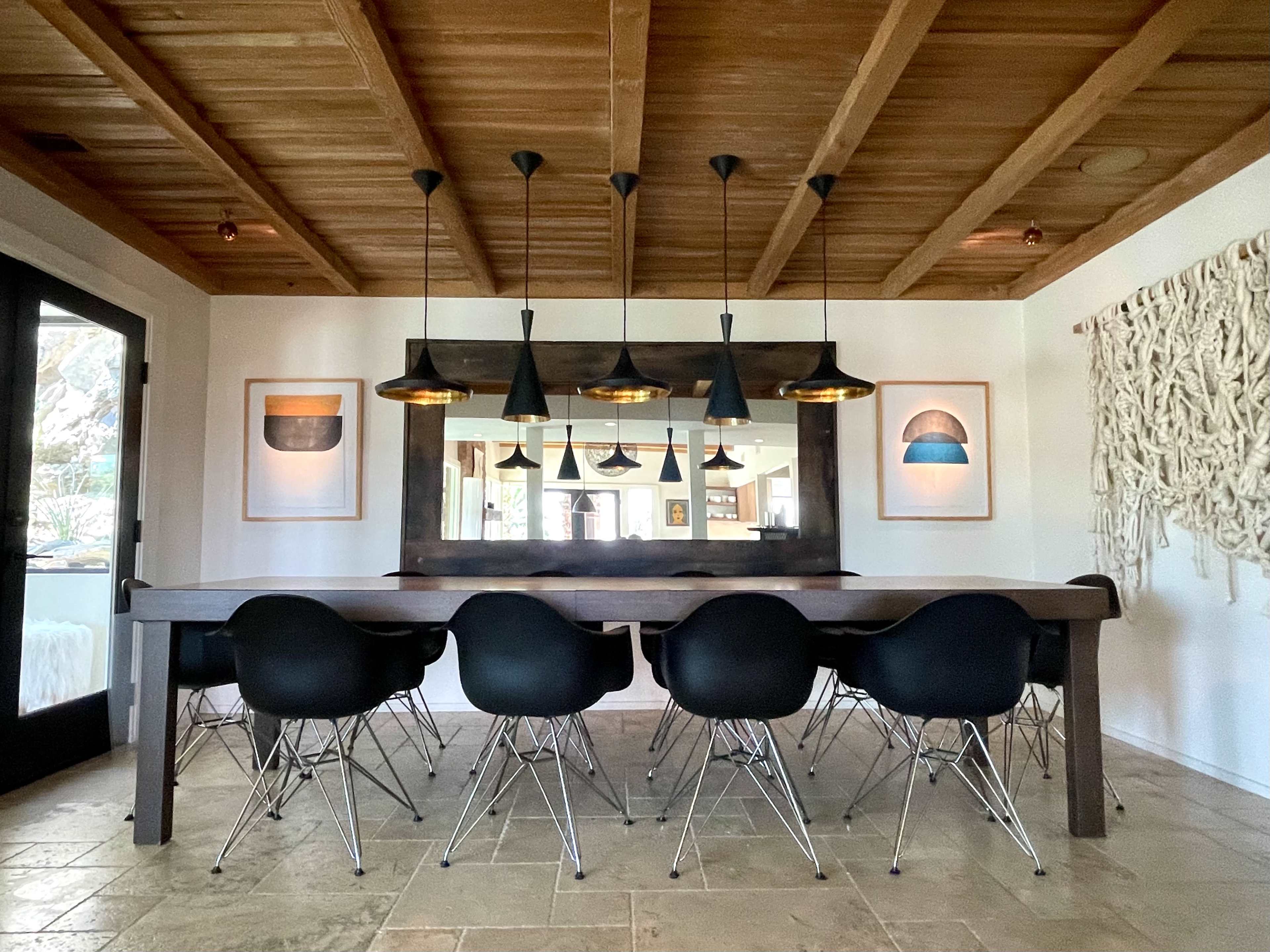 A spacious dining room features a wooden table surrounded by black chairs, complemented by pendant lamps and framed artwork on the walls.