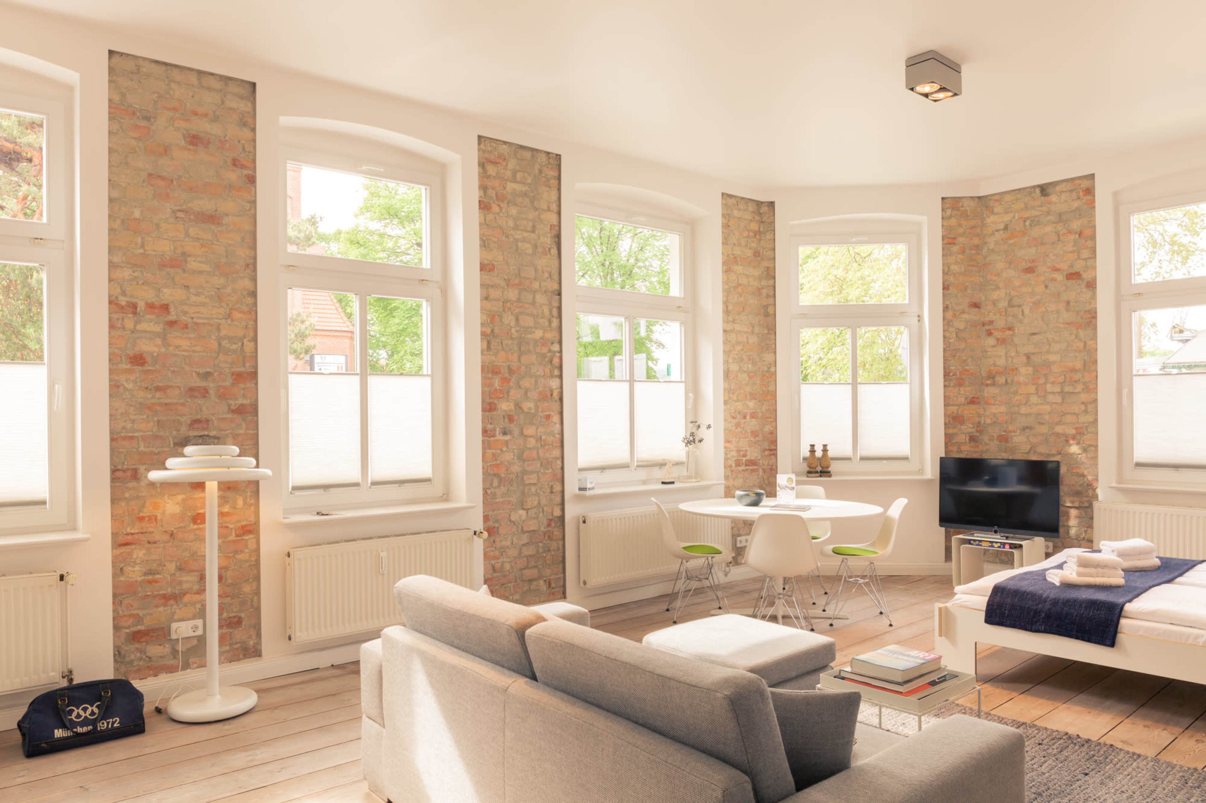 A modern apartment with exposed brick walls, large windows, and a combination of a living area and sleeping space.