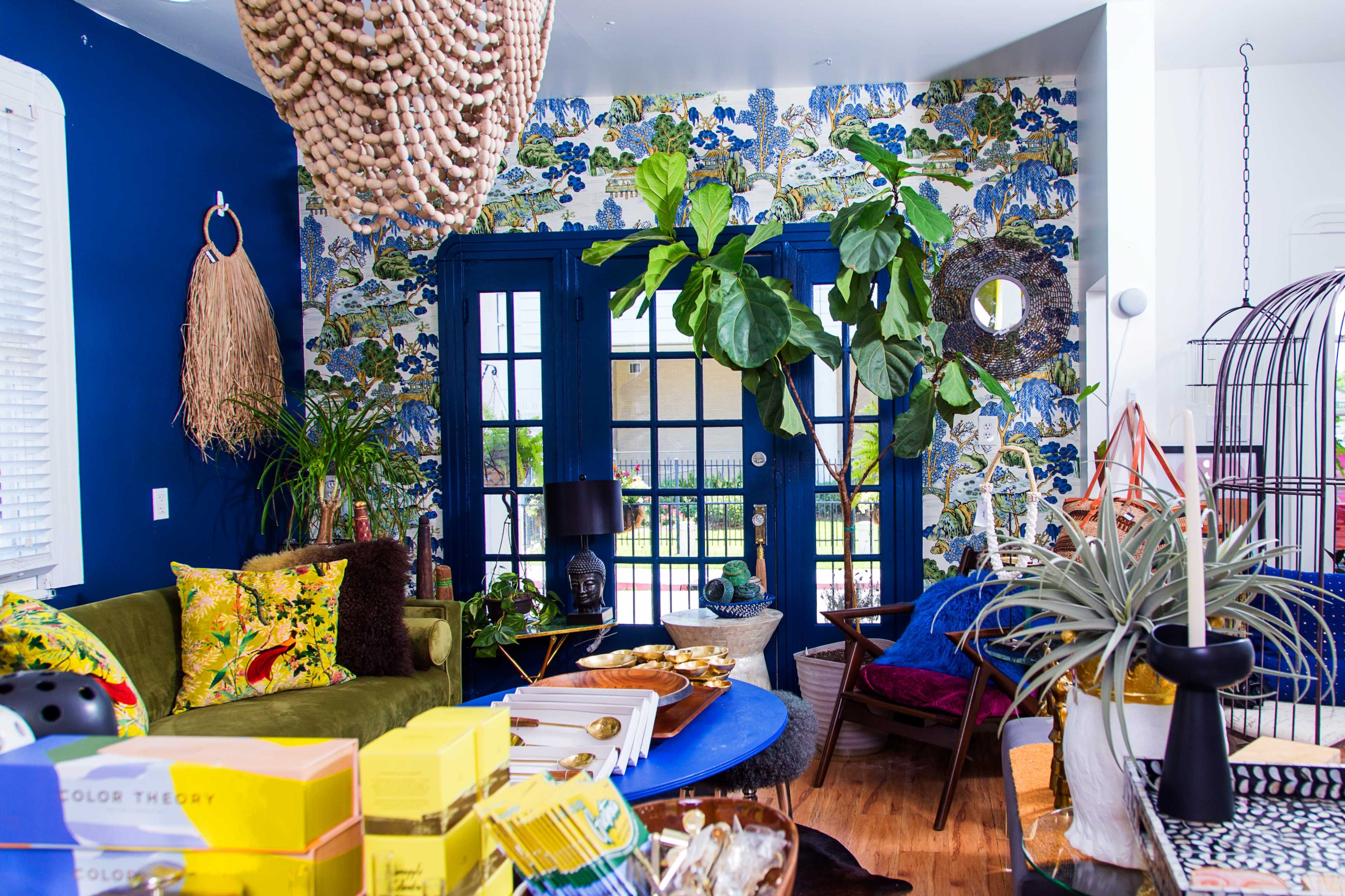 The room features a mix of decorative plants, vibrant furnishings, and patterned wallpaper, creating a cozy living space.