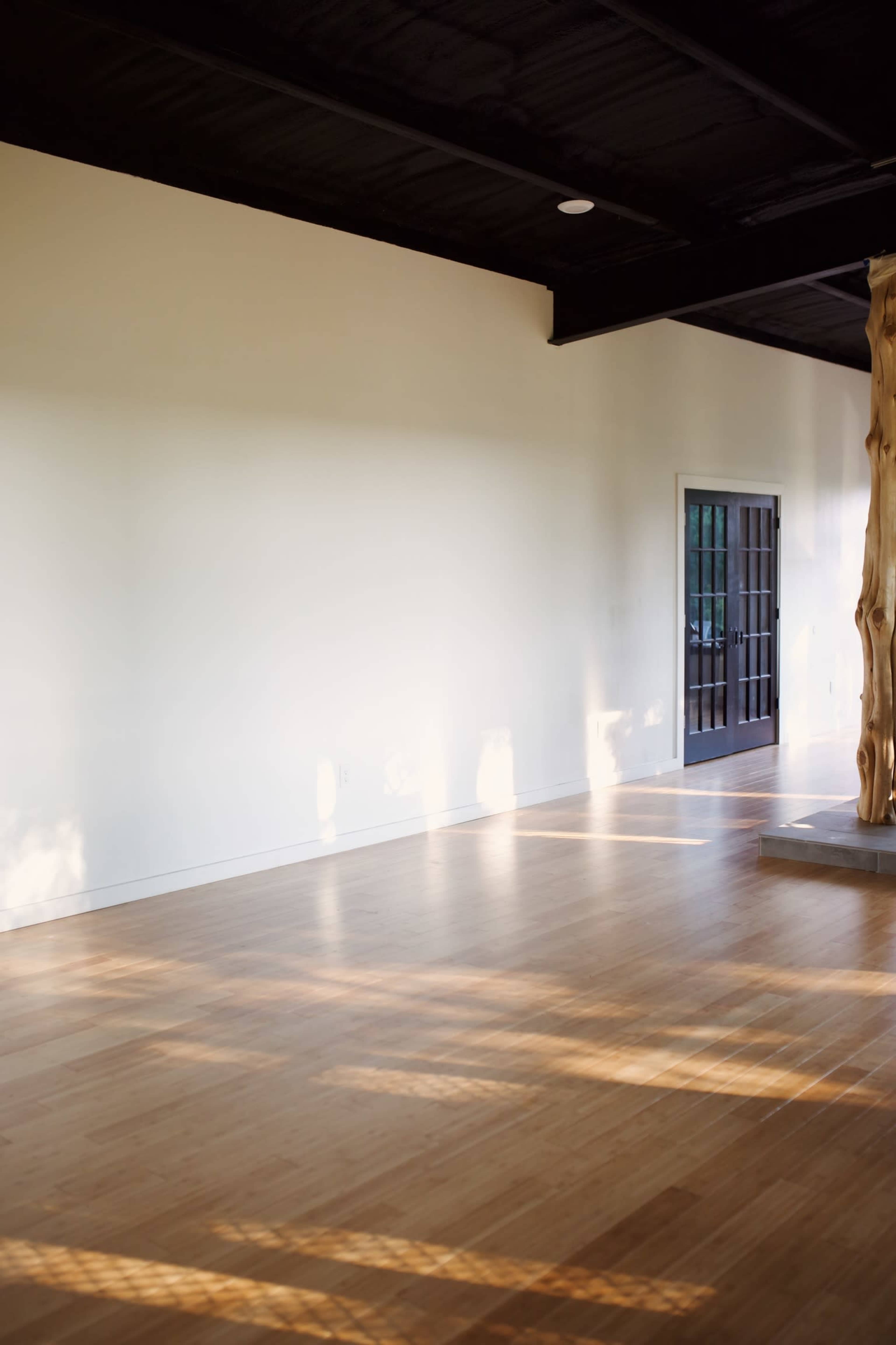 A spacious interior with wooden flooring, a plain white wall, and a doorway framed by a large window.