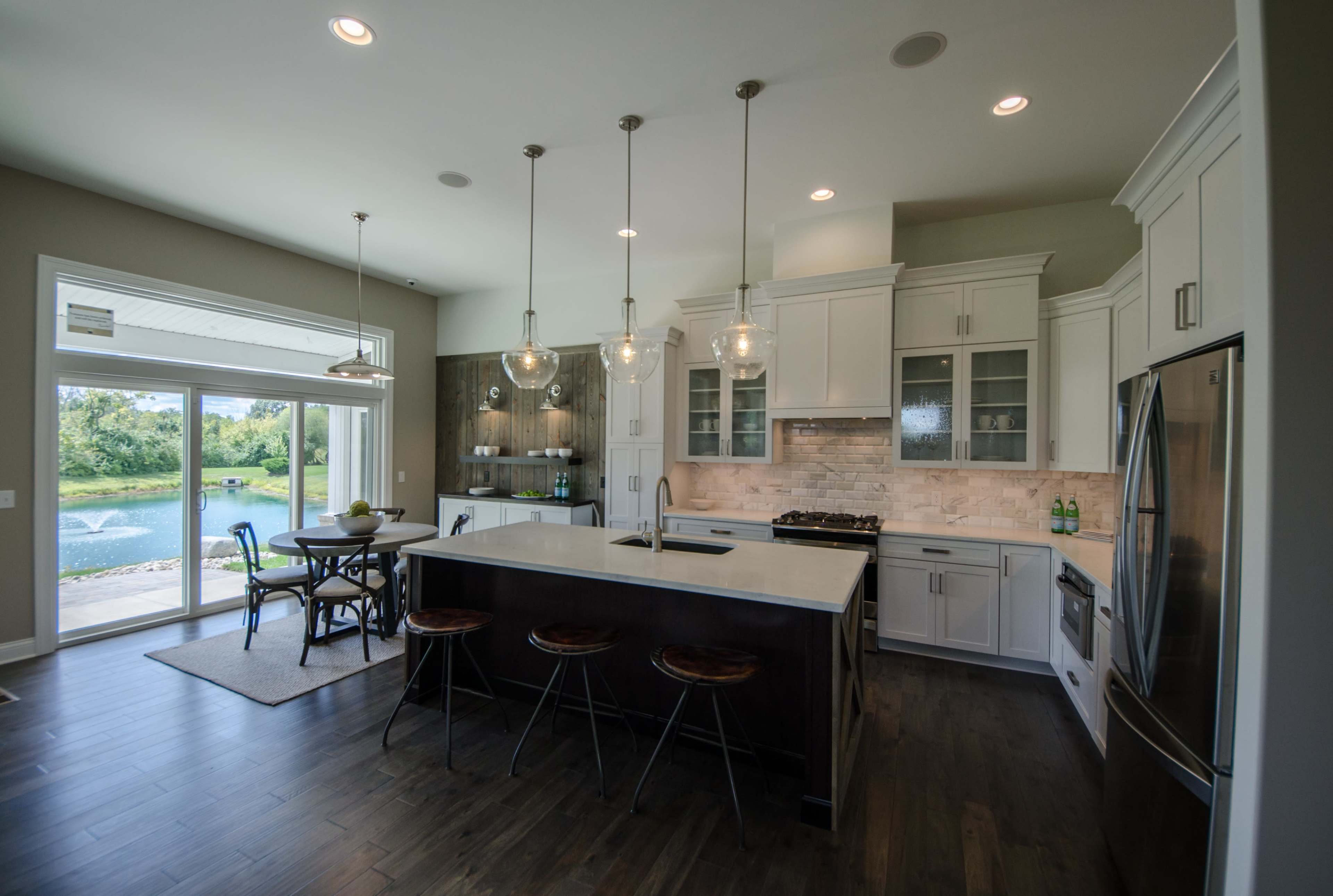 The kitchen features a large island with bar stools, white cabinetry, and a view of a scenic outdoor area through sliding glass doors.