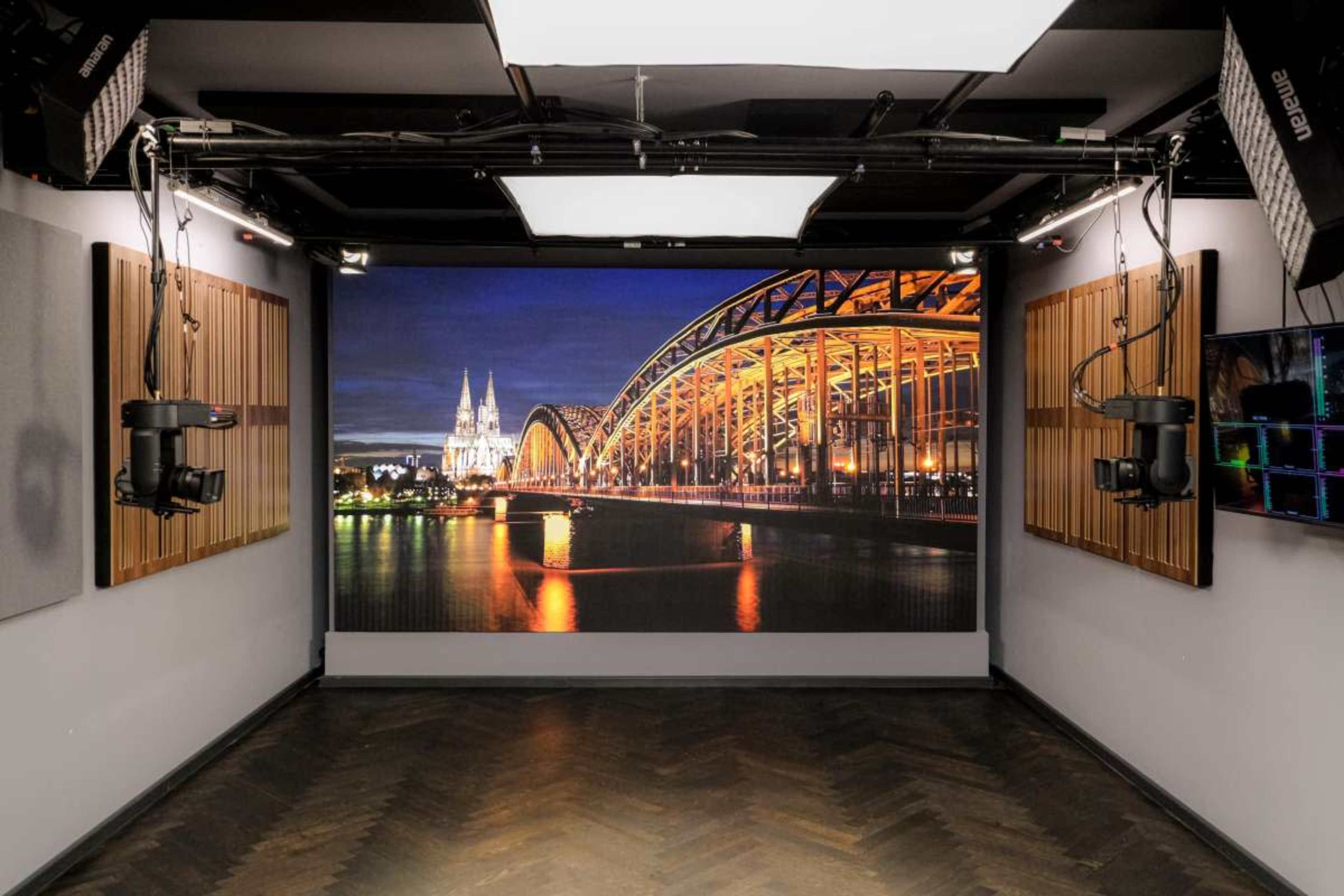 The scene features a studio space with a large illuminated image of a bridge and a city skyline on the back wall, surrounded by sound panels and camera equipment.