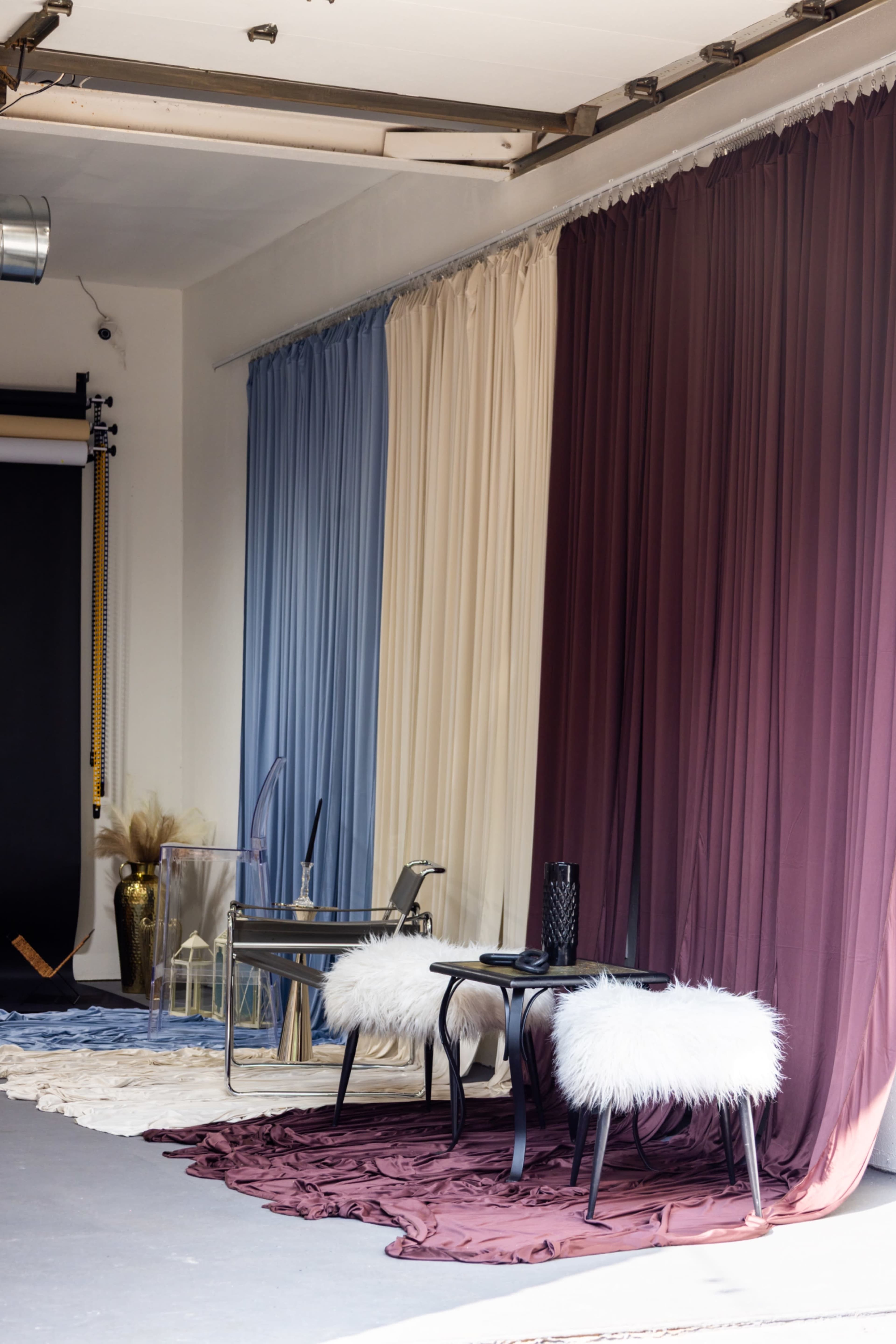 The image shows a room with draped fabric in various colors and two tables with fluffy white seating.