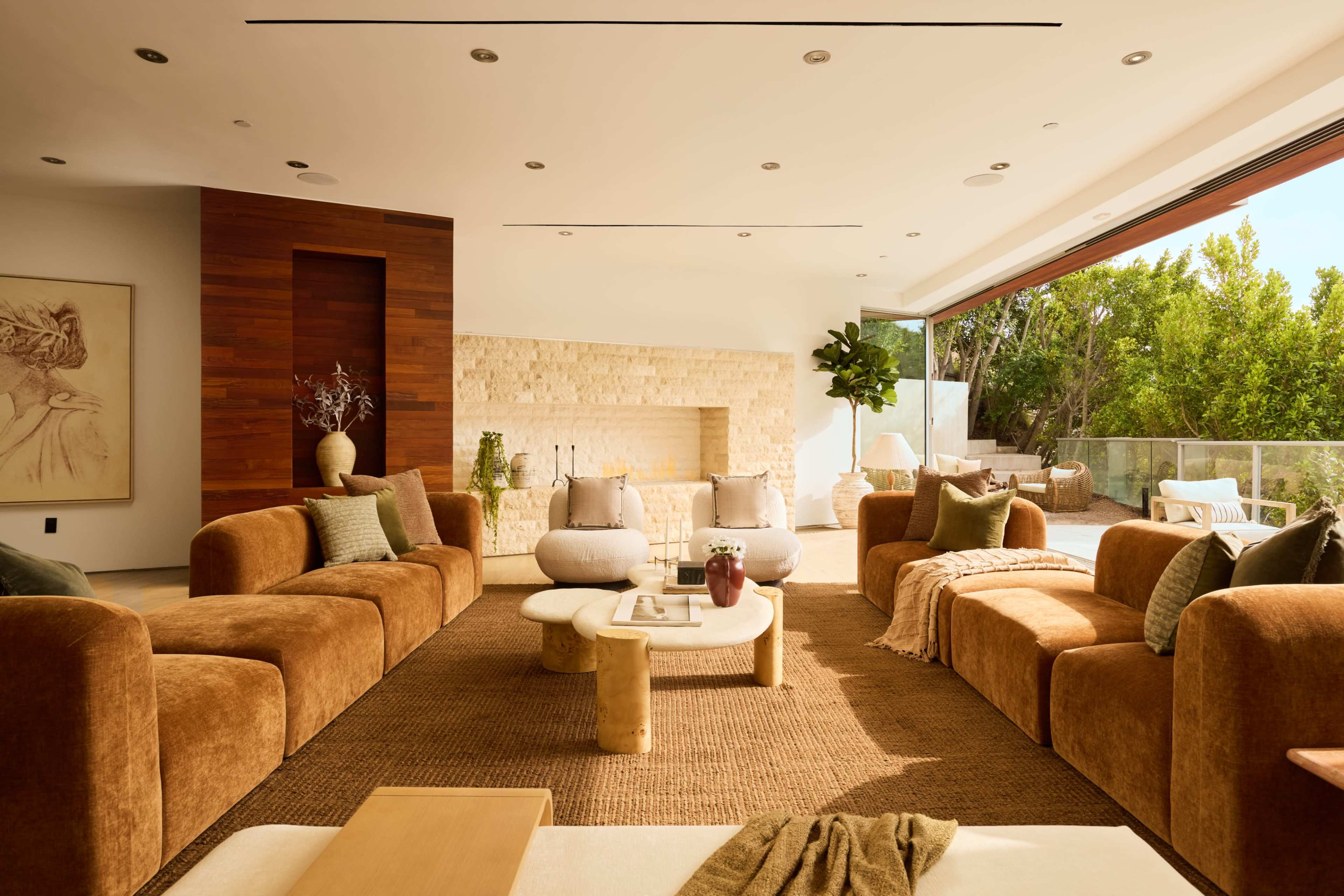 The living room features brown seating, a light-colored coffee table, and large glass doors that open to a garden area.
