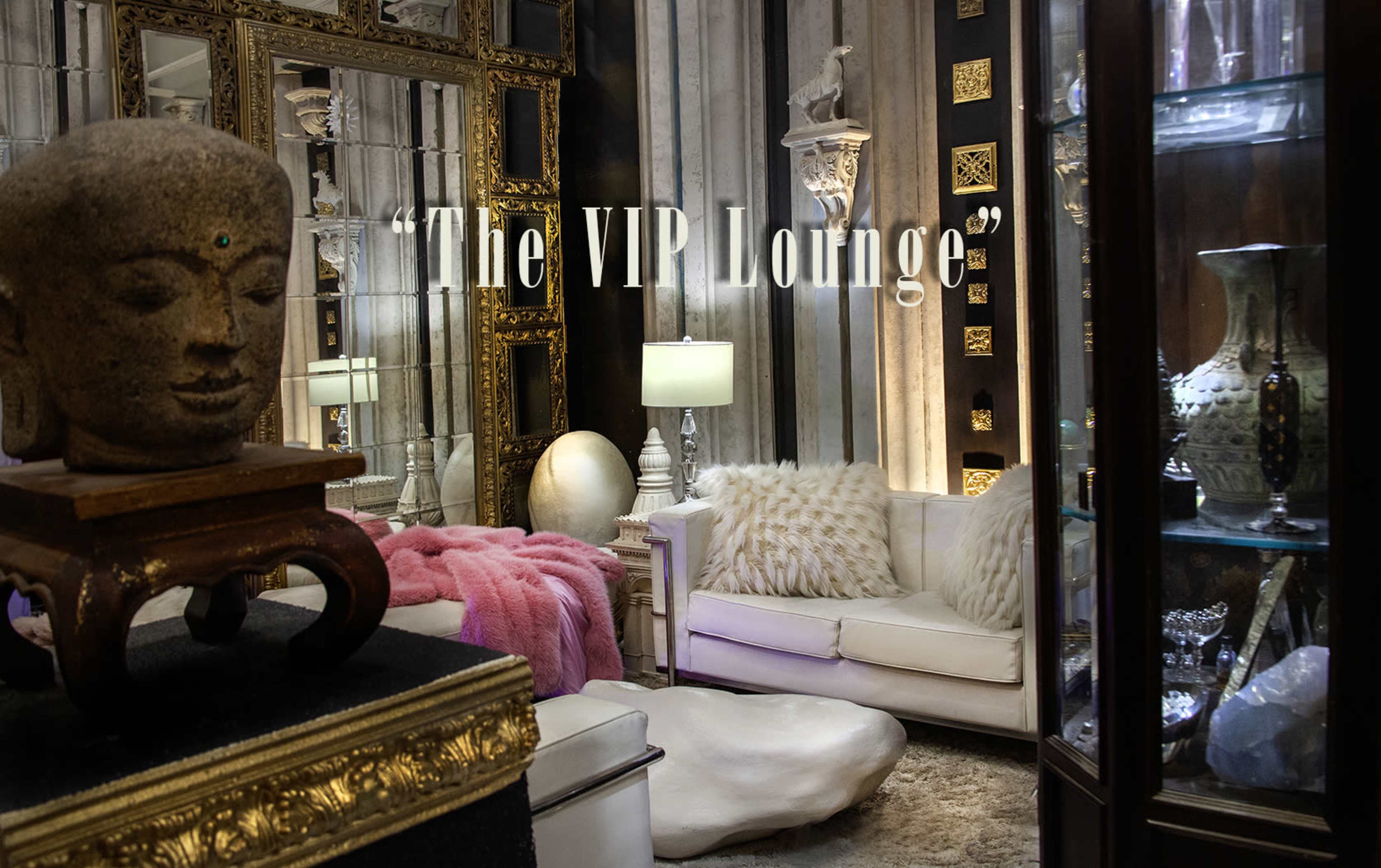 The image depicts an elegantly decorated lounge area featuring a mix of furnishings, including a white sofa, decorative sculptures, and glass display cabinets.