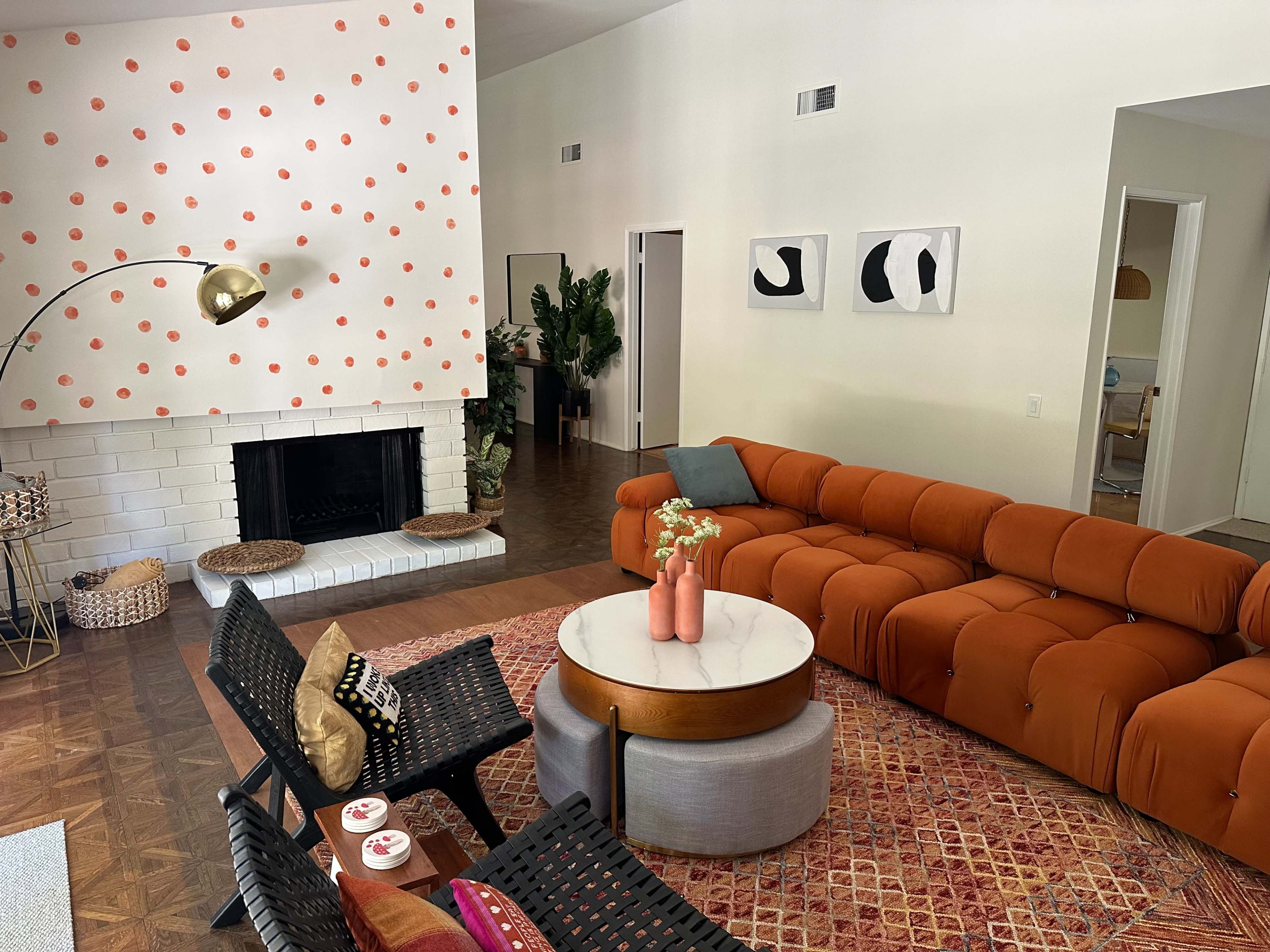 The living room features an orange sectional sofa, a round coffee table with pink vases, and a fireplace against a wall decorated with pink dots.