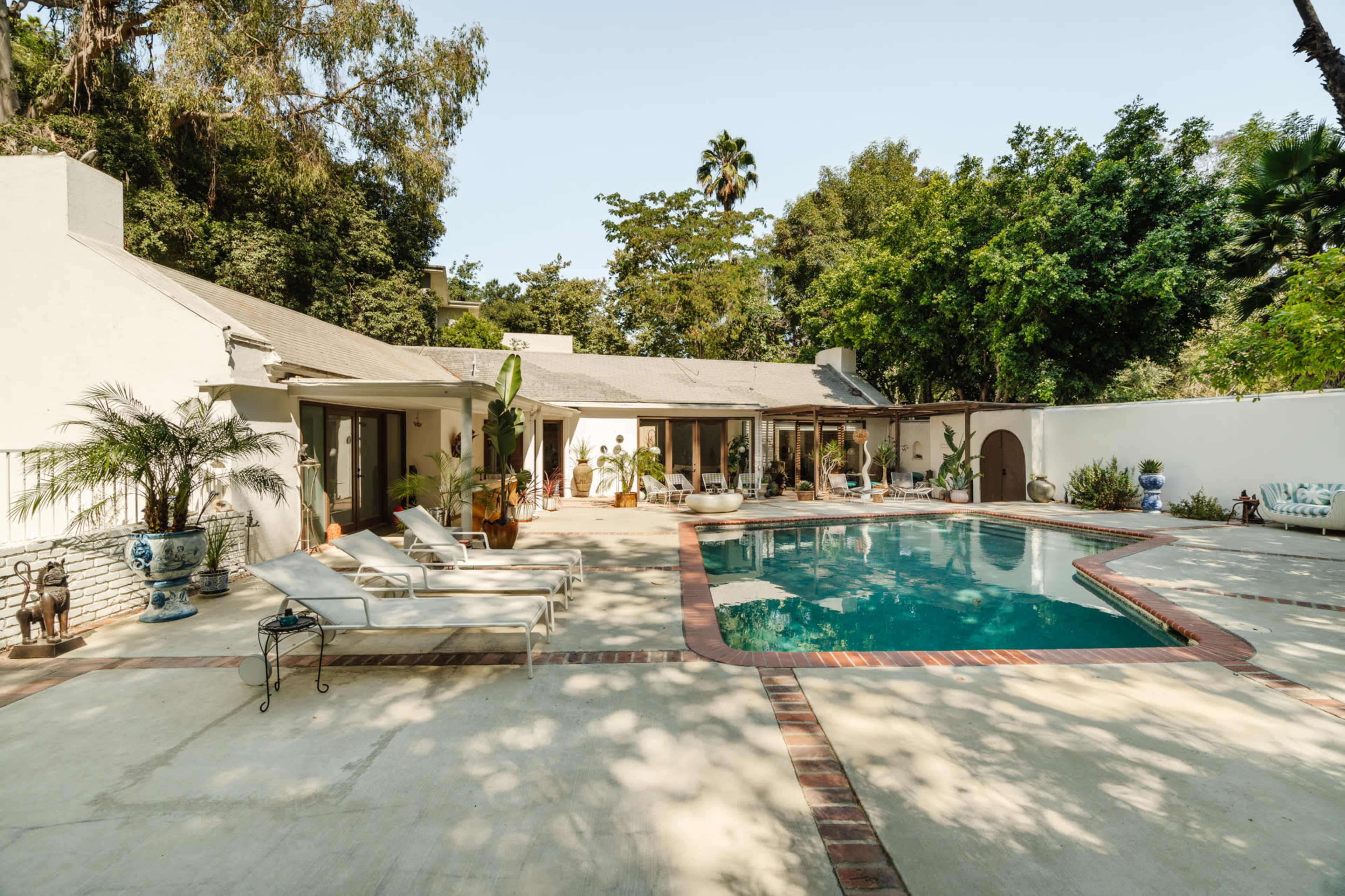 A spacious backyard features a swimming pool surrounded by lounge chairs and lush greenery.
