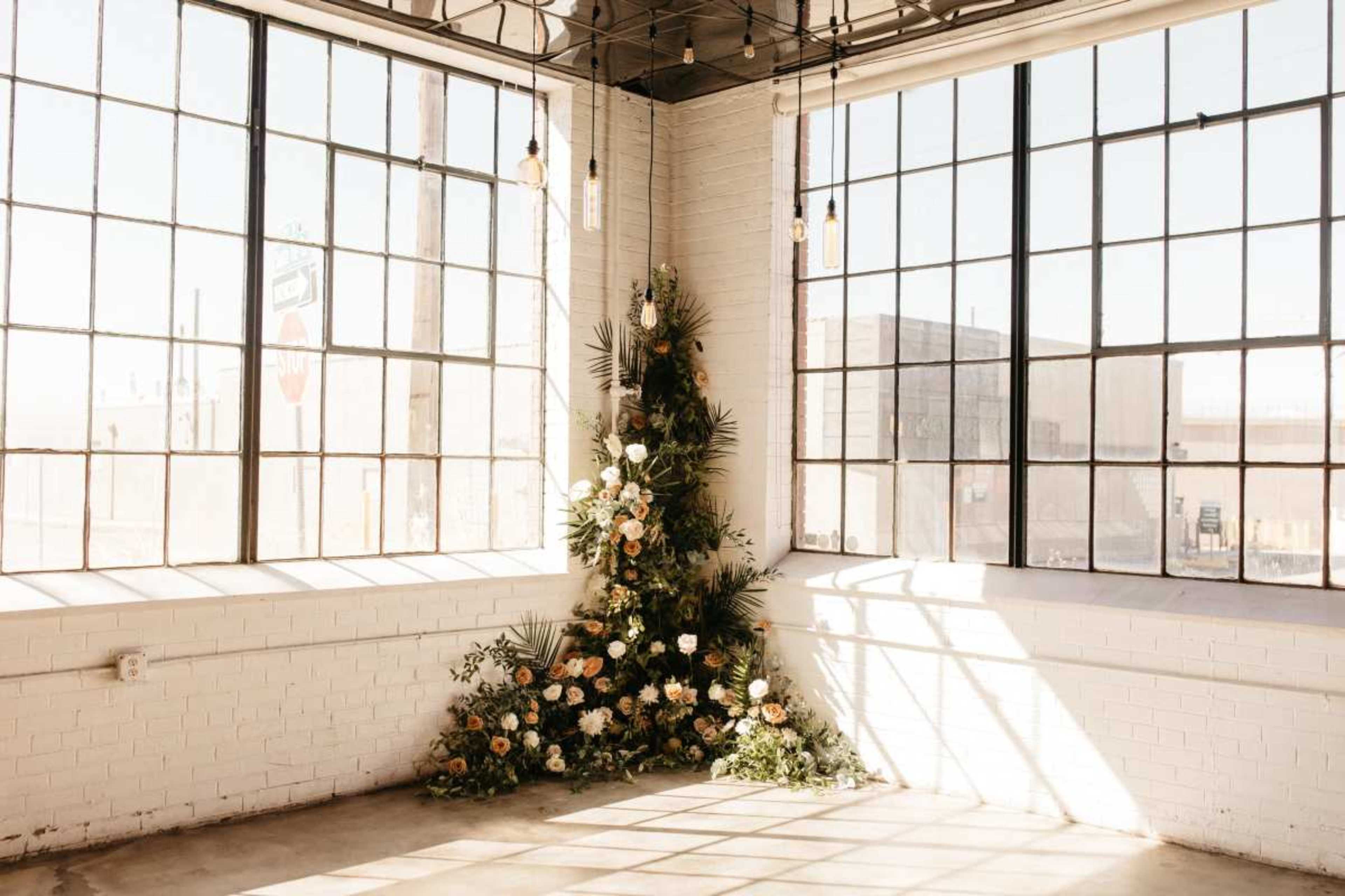 The image shows a bright, spacious room with large windows and a floral arrangement in the corner.