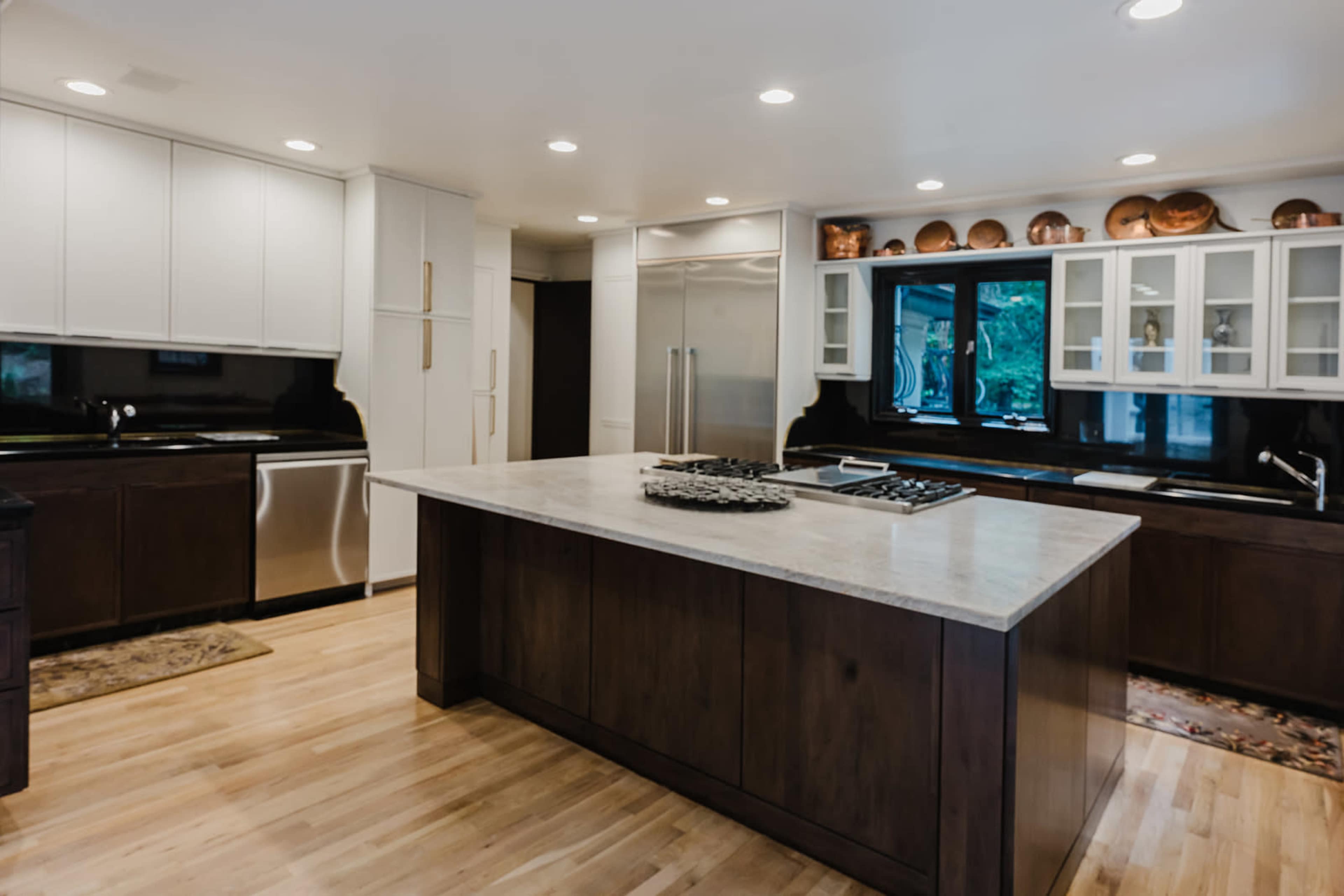 The kitchen features a large central island with a marble countertop, dark wooden cabinetry, and modern appliances.