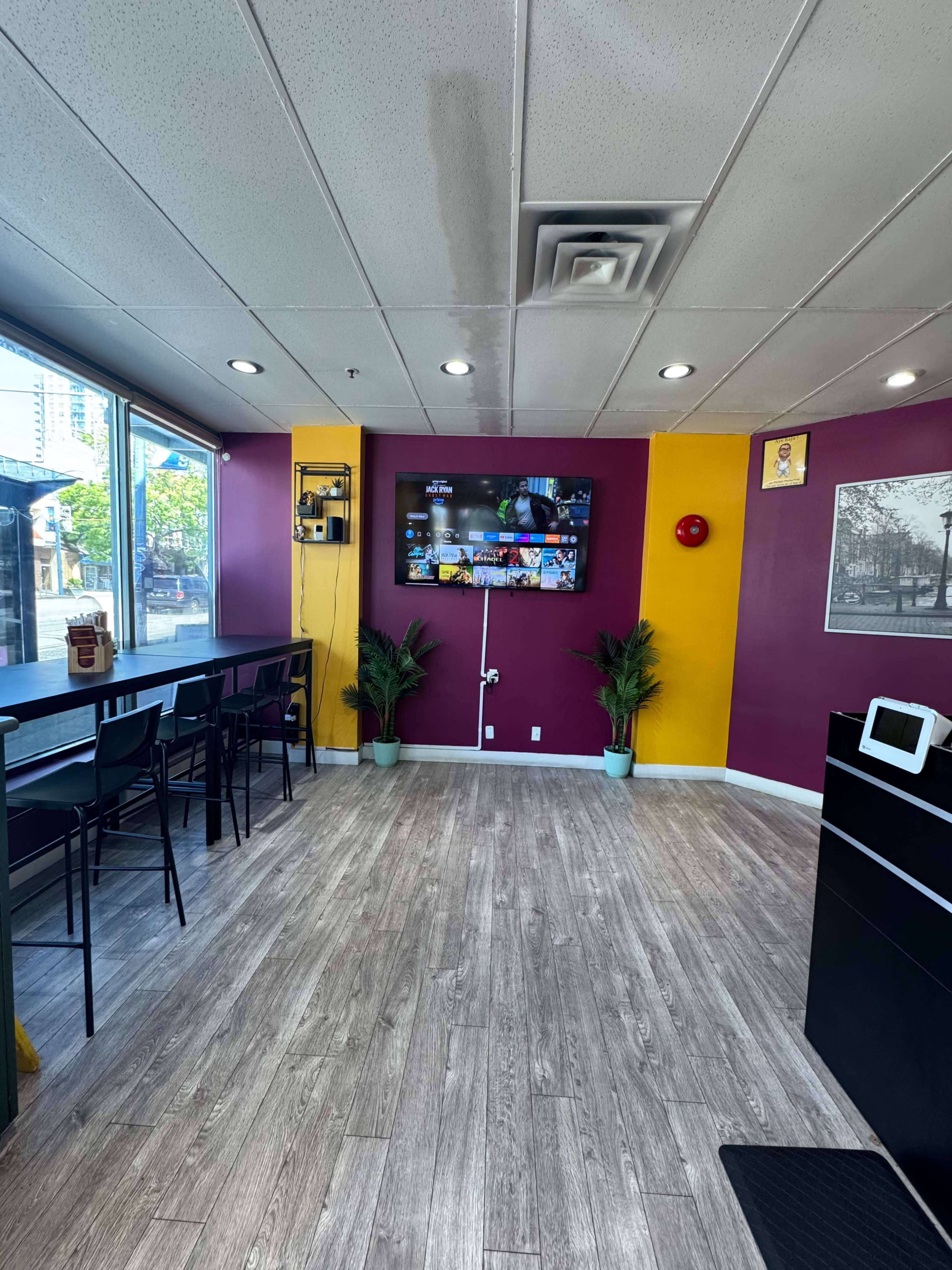 The image shows a brightly colored café interior with purple and yellow walls, a television mounted on the wall, and seating along one side.