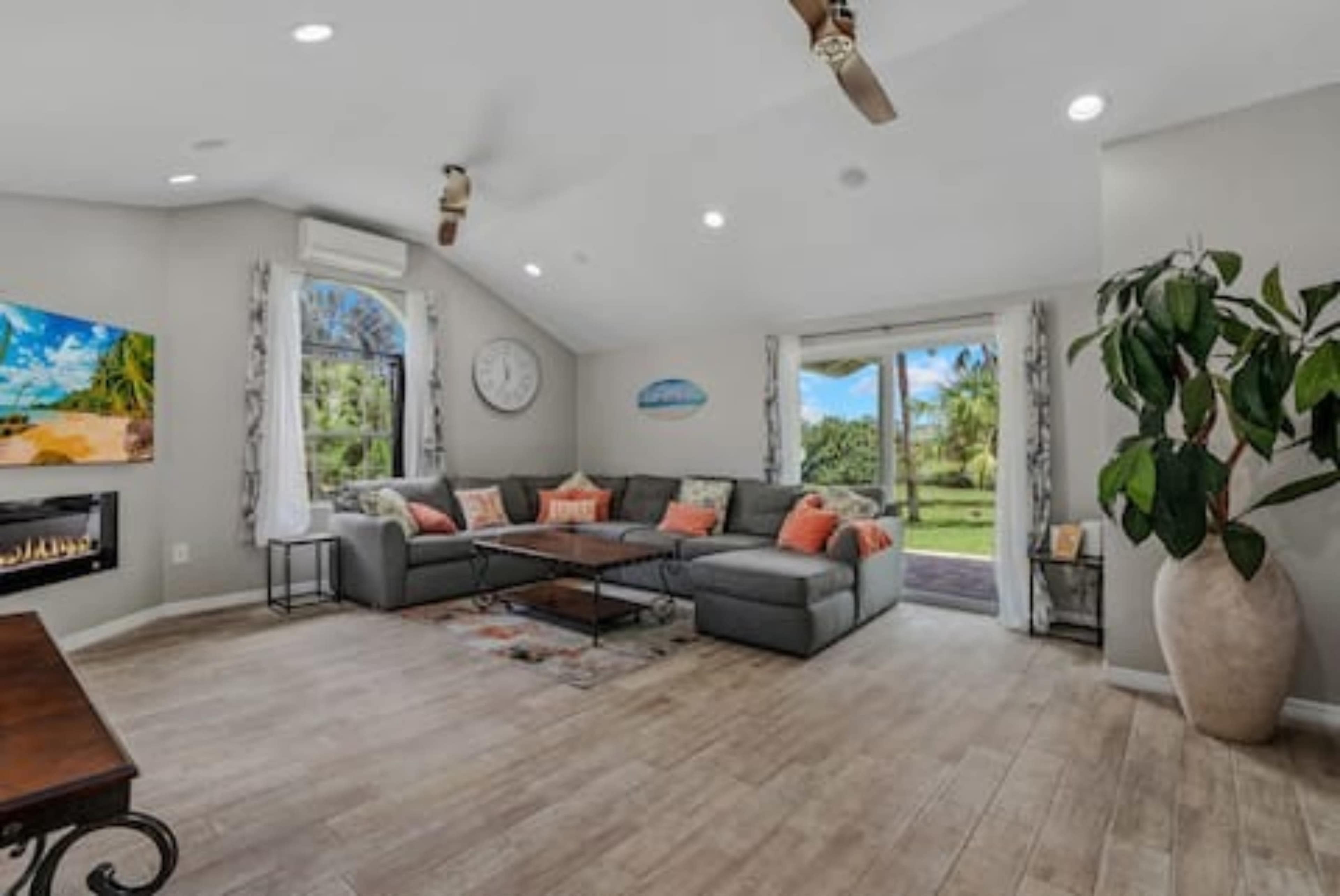 The image shows a well-lit living room featuring a large gray sectional sofa, a coffee table, and a door leading to a green outdoor area.