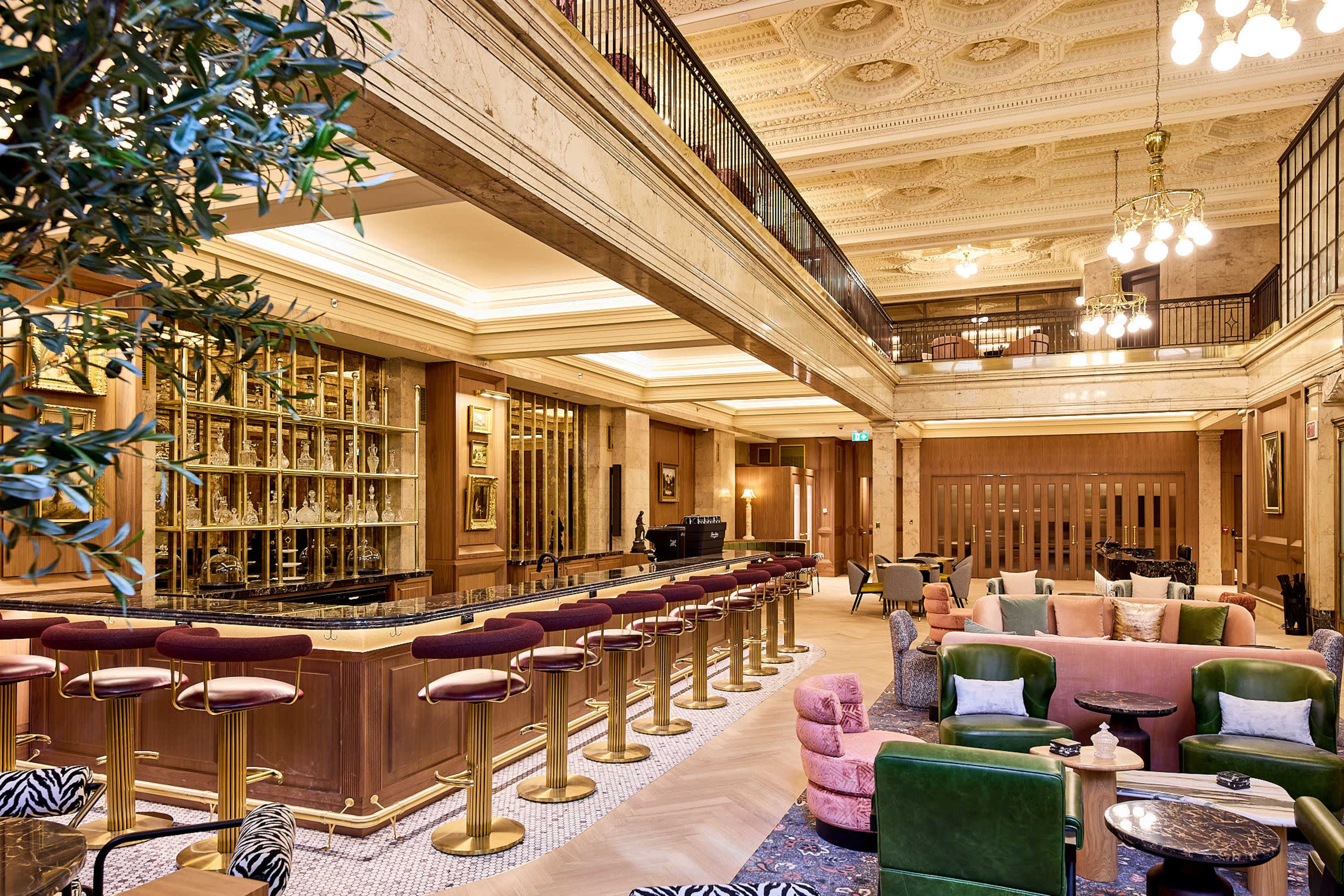 The image shows an elegant bar area within a beautifully designed lounge, featuring a marble counter, plush seating, and ornate architectural details.