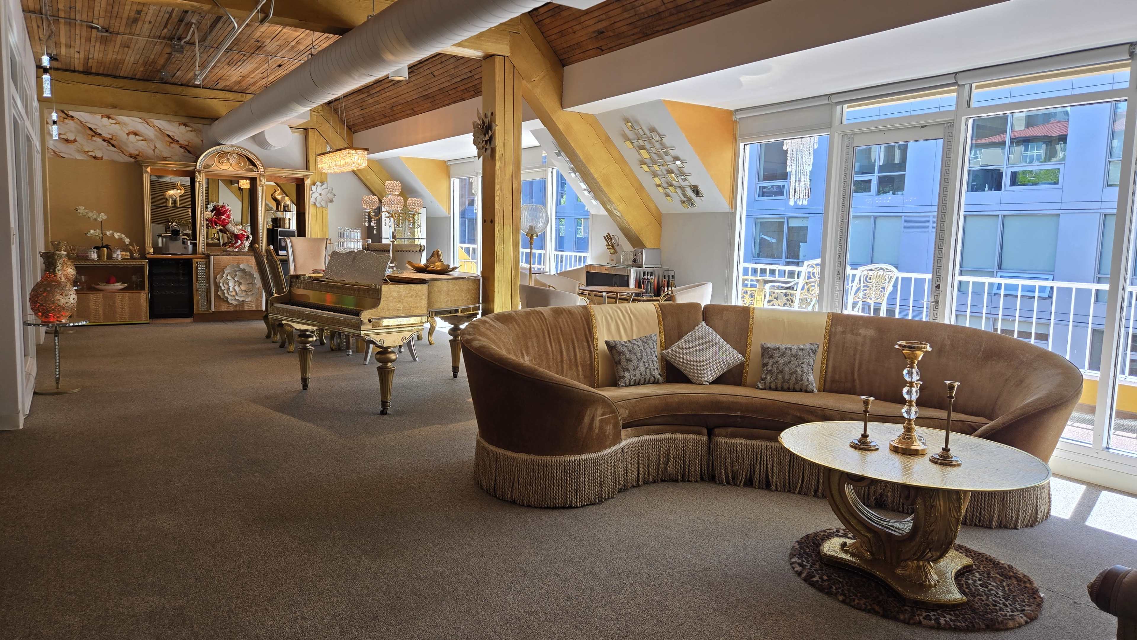The image shows a spacious, stylishly decorated living area with a curved sofa, a piano, and large windows that allow natural light to enter.