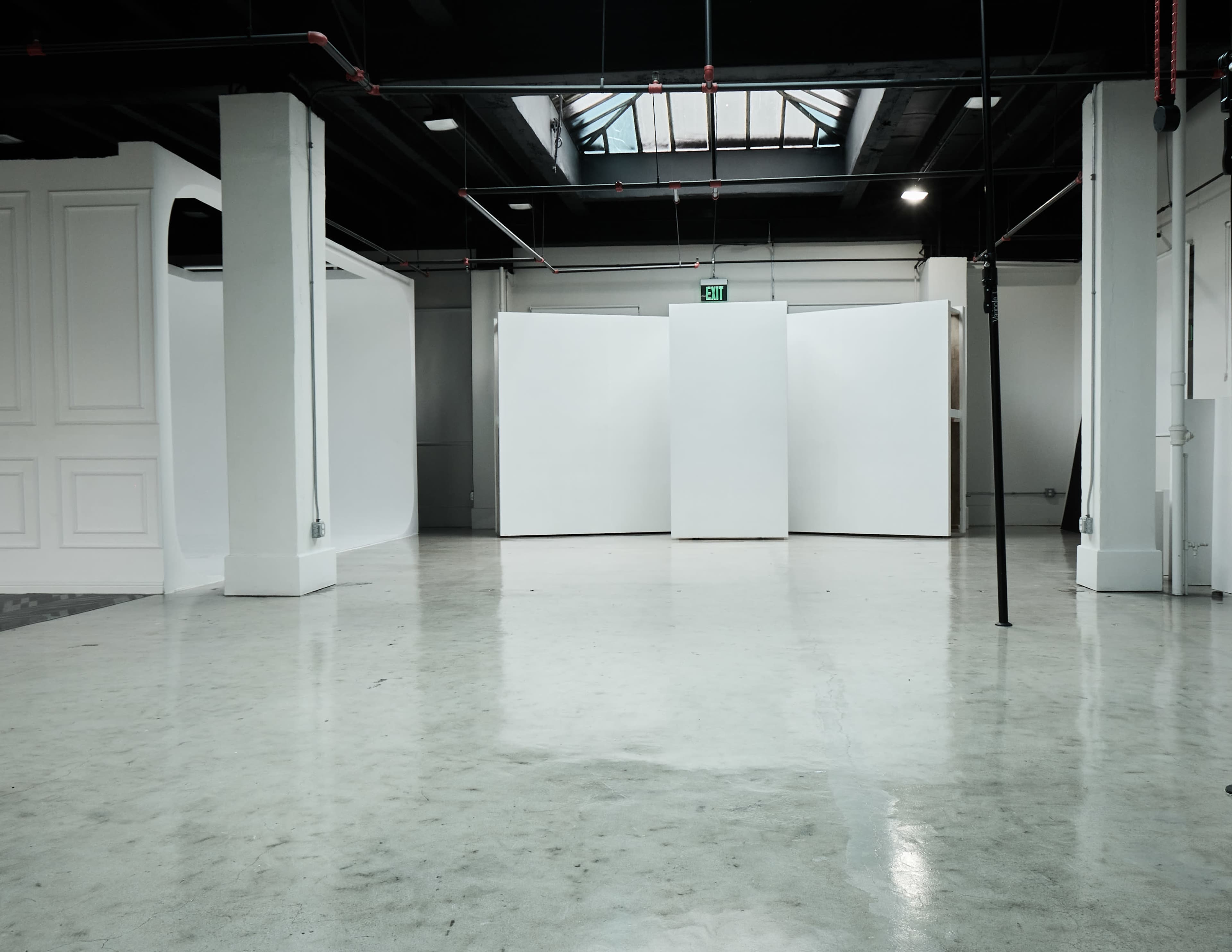 The image shows an empty gallery space with white walls and a polished concrete floor.
