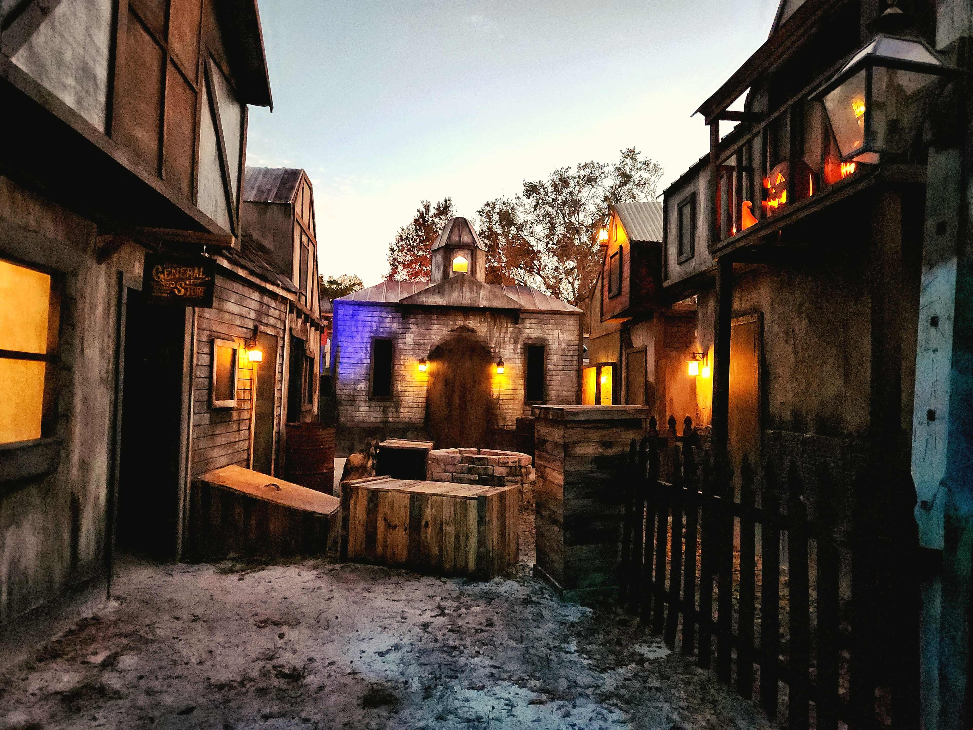 The image depicts a vintage-style street scene with rustic buildings, lanterns illuminating the surroundings, and a central well.