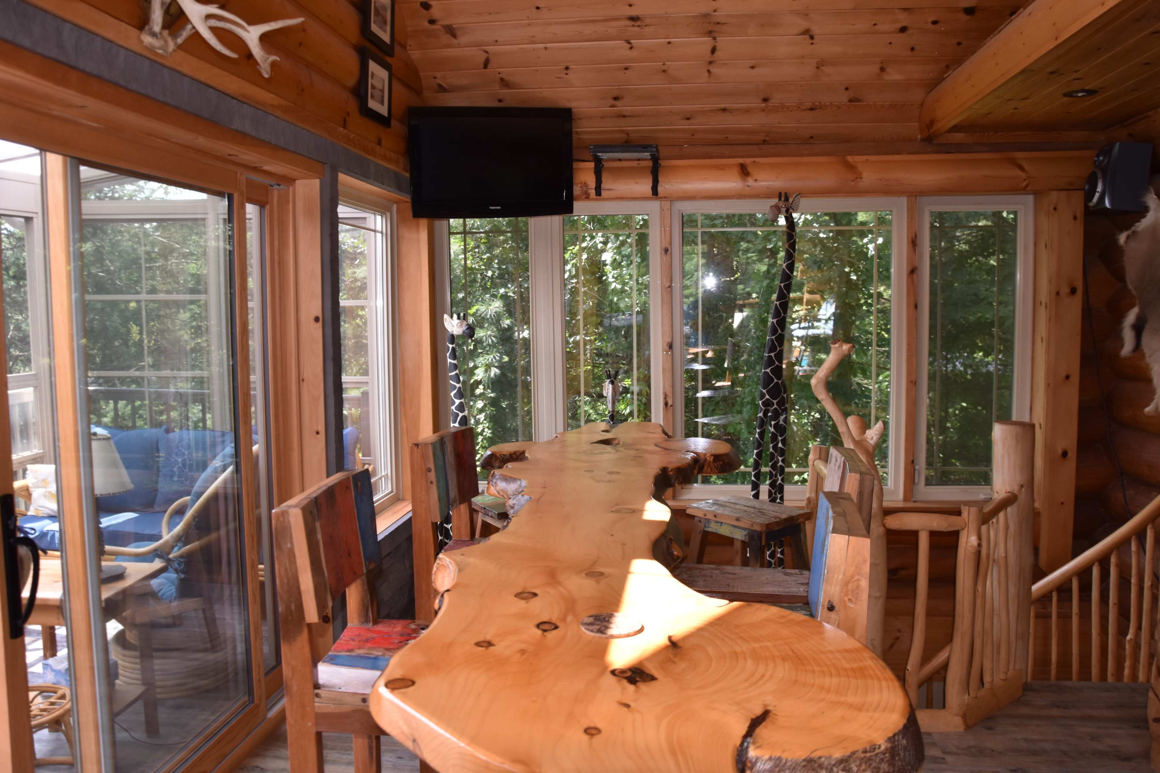 A wooden table in a sunlit room with large windows overlooking greenery.