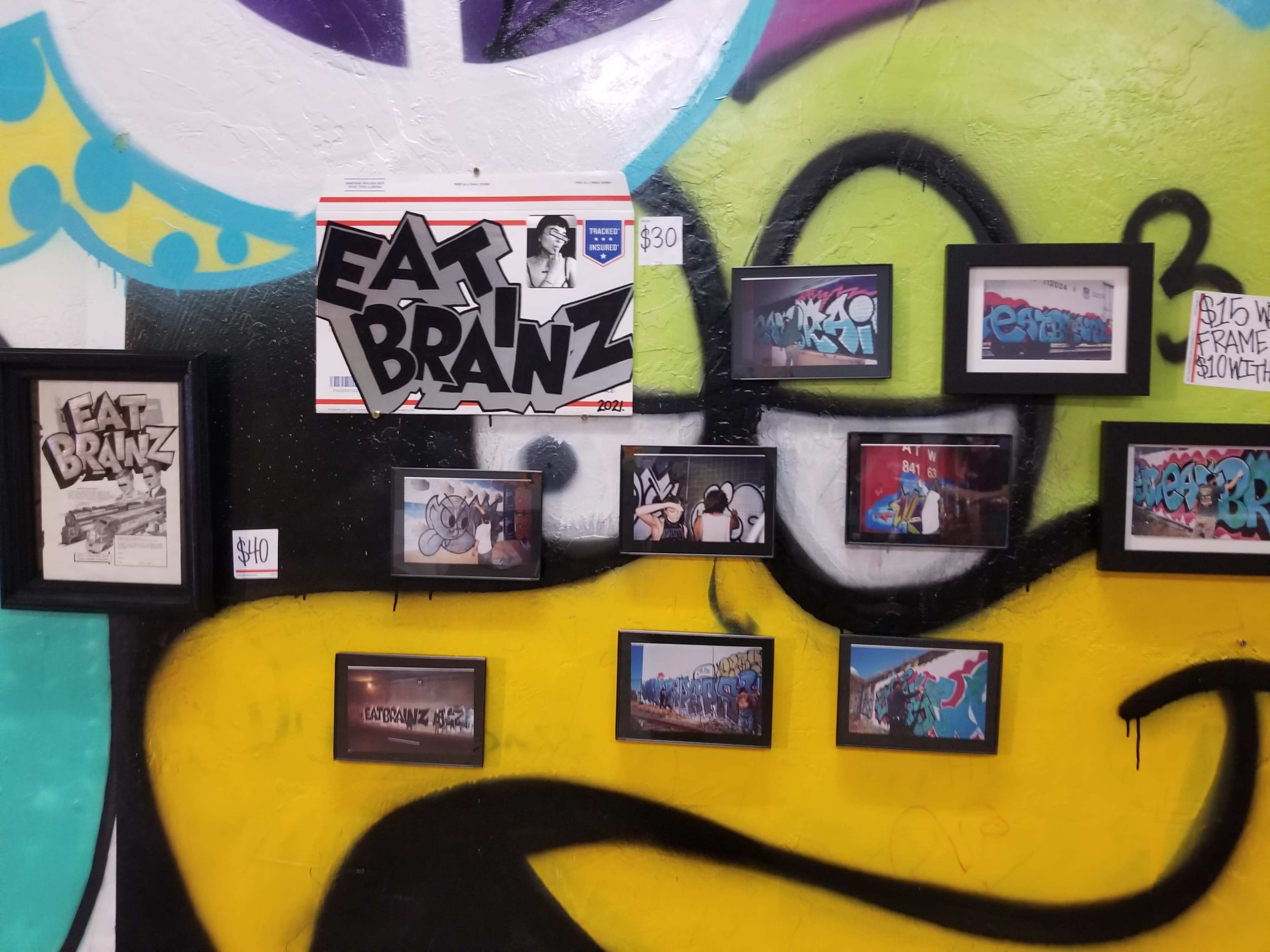 A colorful wall mural featuring various framed graffiti artworks and a large poster that reads "EAT BRAHNZ."