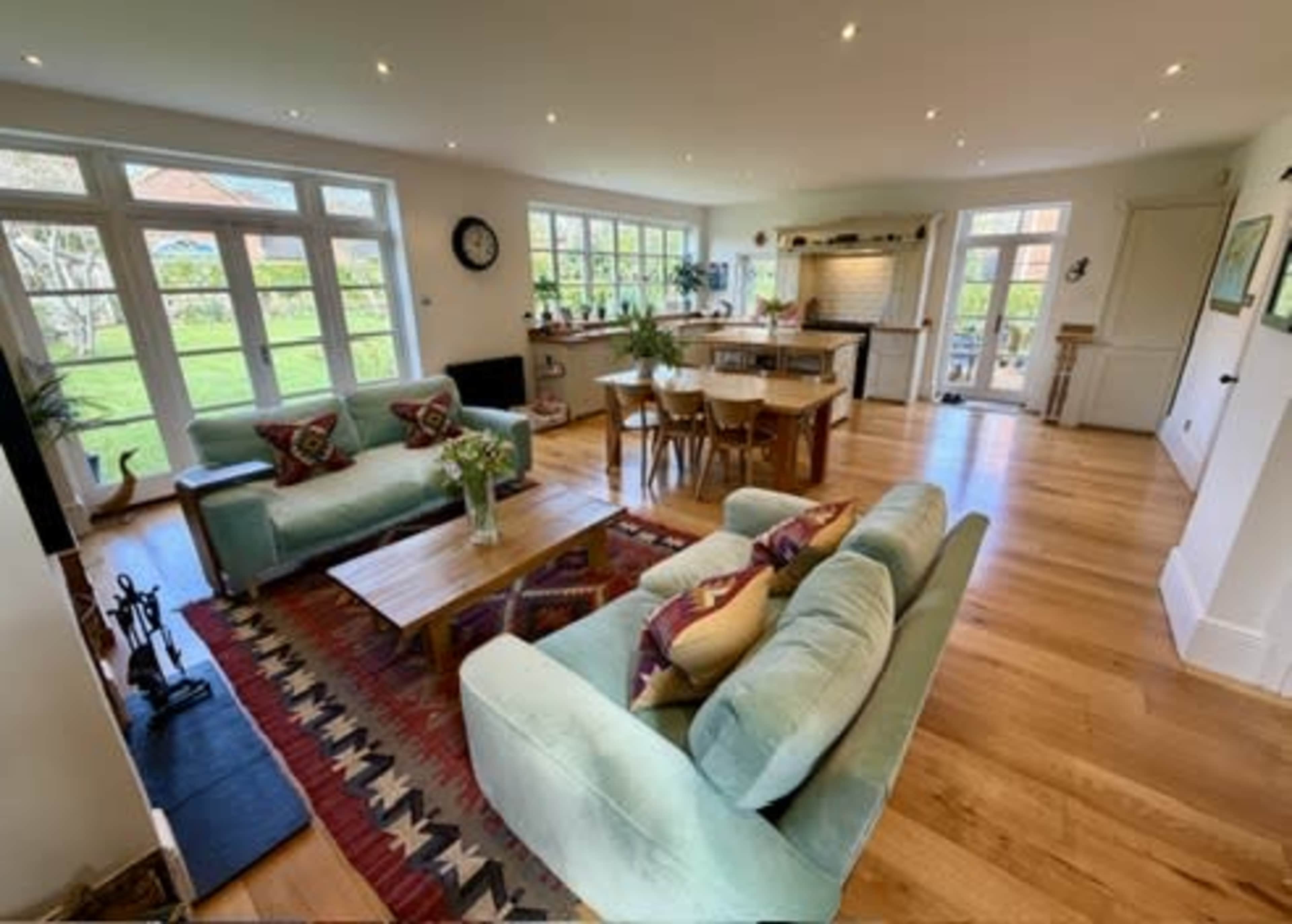 The image shows a bright and spacious open-plan living area with two sofas, a wooden coffee table, and large windows allowing natural light to stream in.