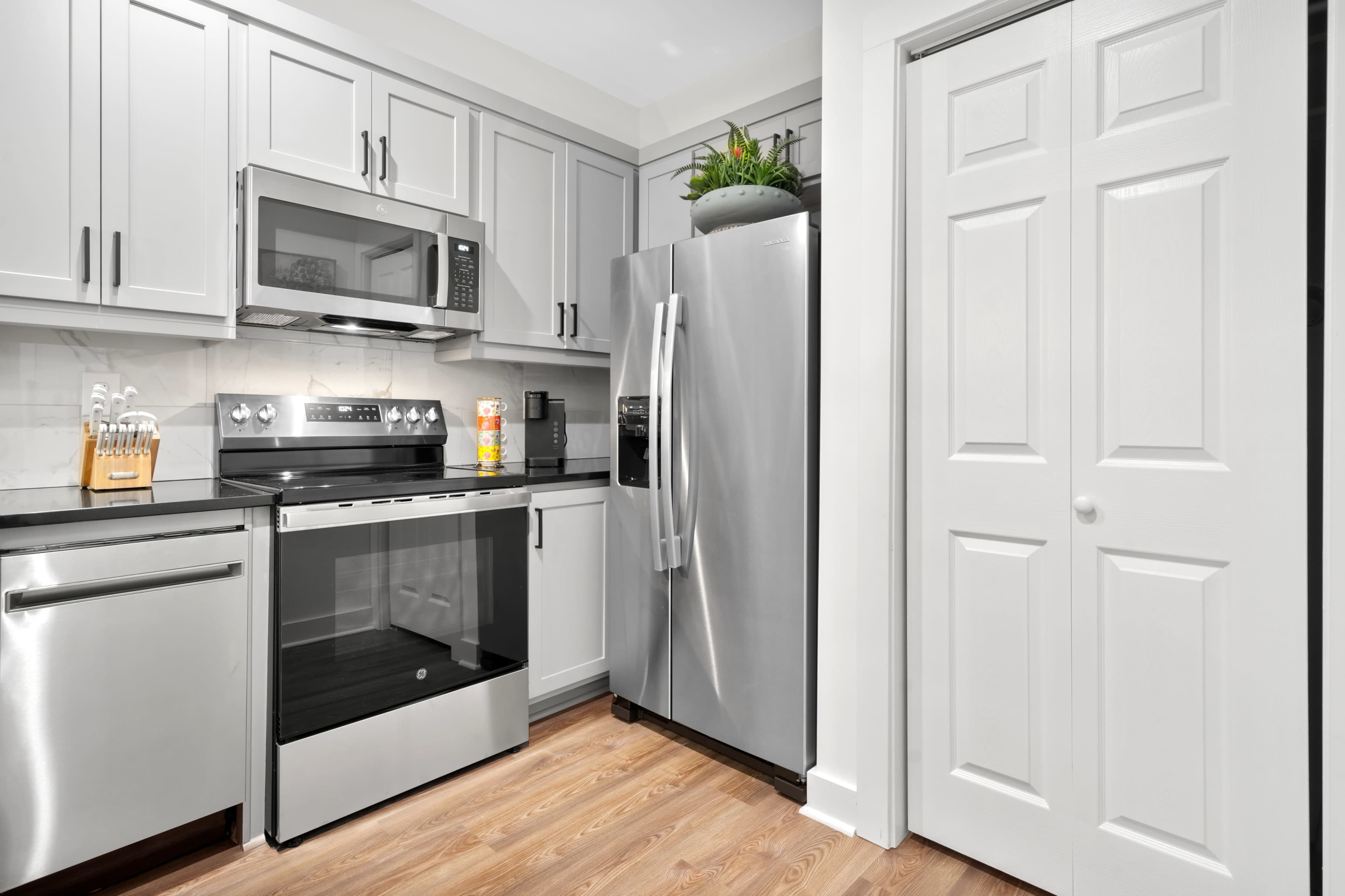 The image shows a modern kitchen featuring stainless steel appliances, gray cabinets, and a door leading to a closet.