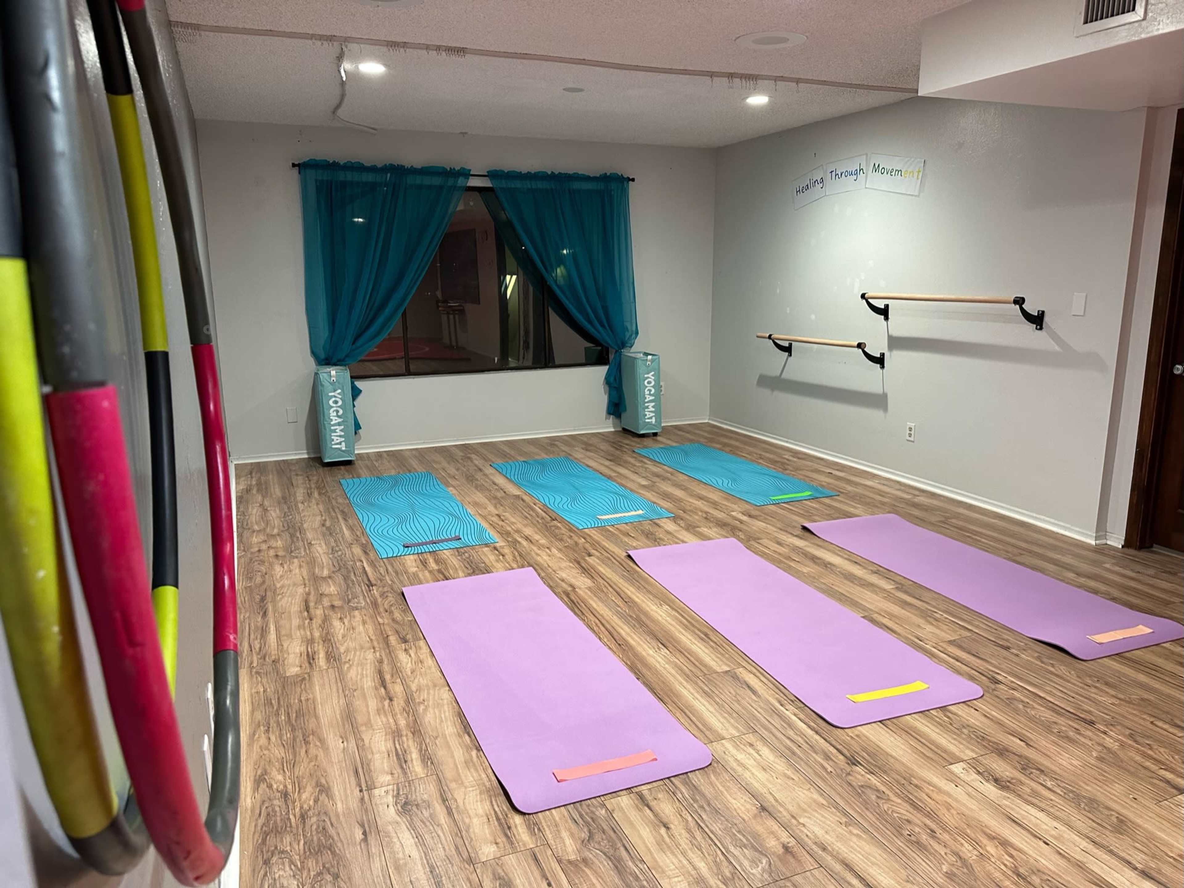 A fitness studio with several exercise mats arranged on a wooden floor, alongside a mirrored wall and colorful props on display.