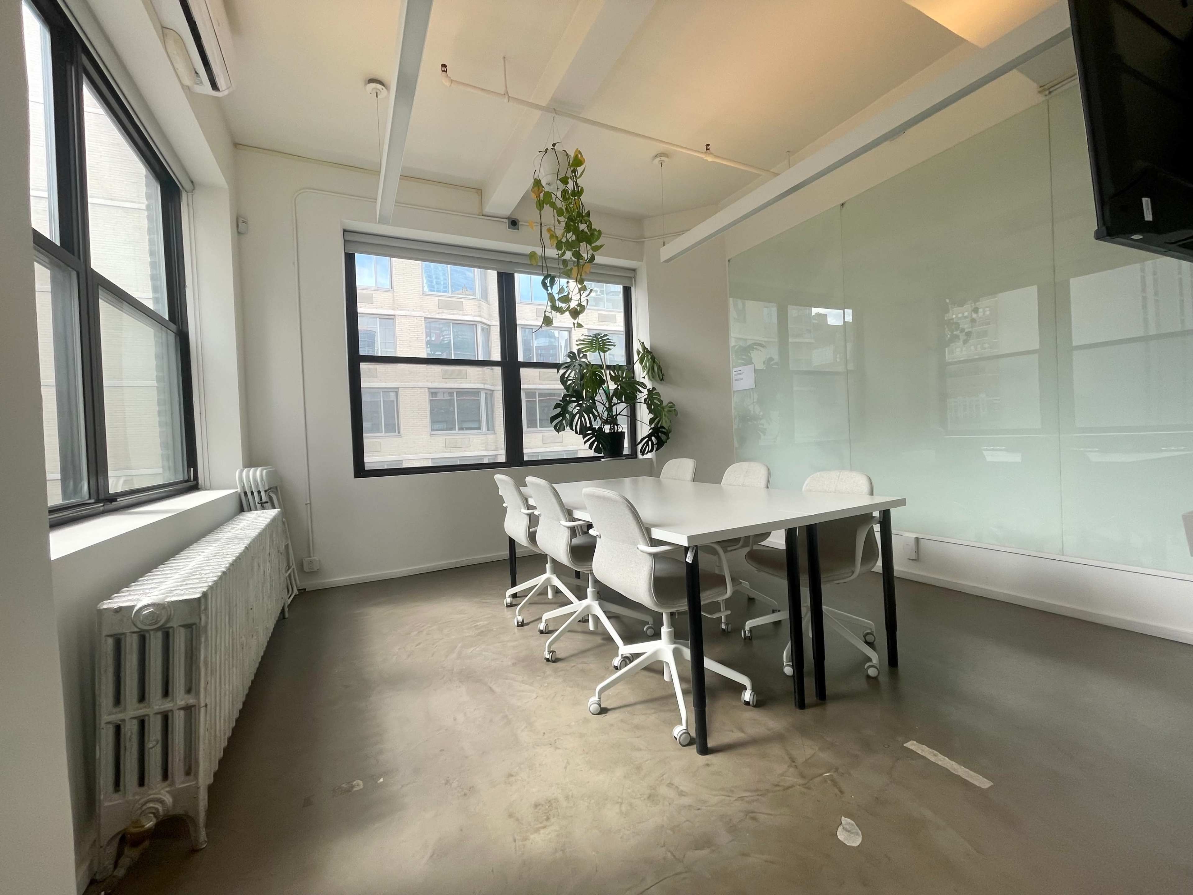A spacious meeting room features a large table surrounded by ergonomic chairs, with large windows allowing natural light and a view of nearby buildings.