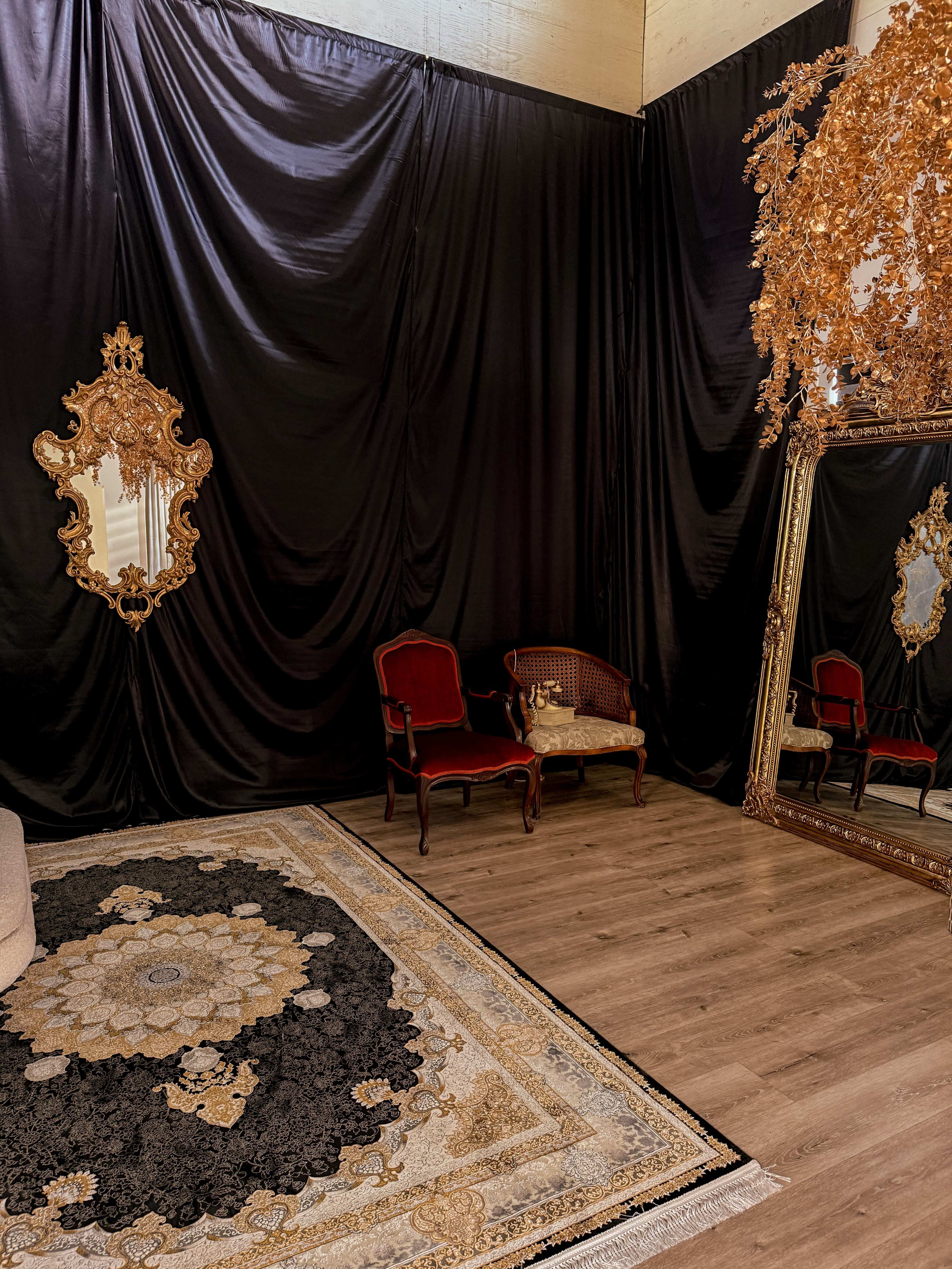 The image shows a room with black draped fabric on the walls, a large ornate mirror, a small couch, and a decorative rug on the wooden floor.