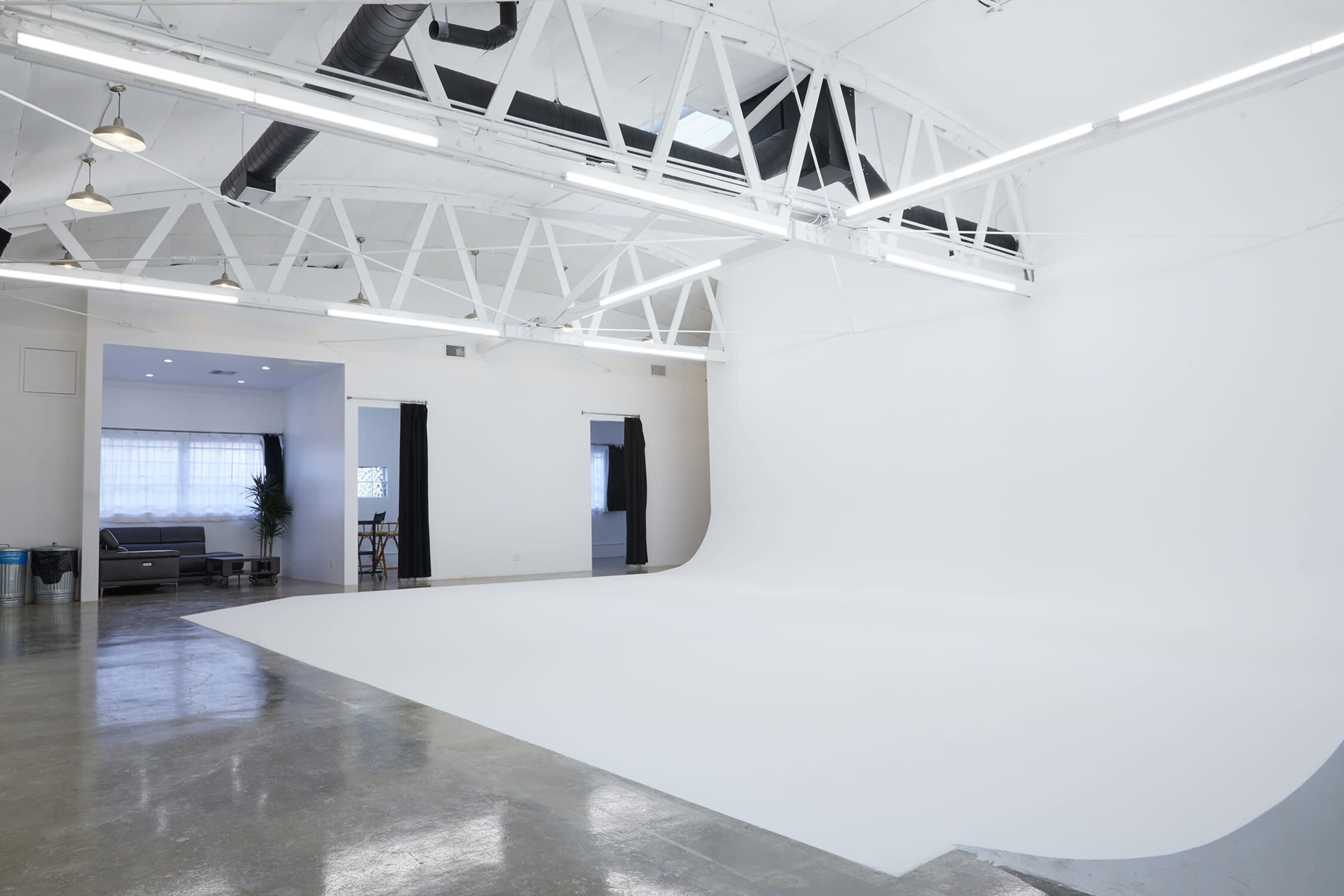 A spacious white photo studio with high ceilings, exposed beams, and a seamless backdrop.