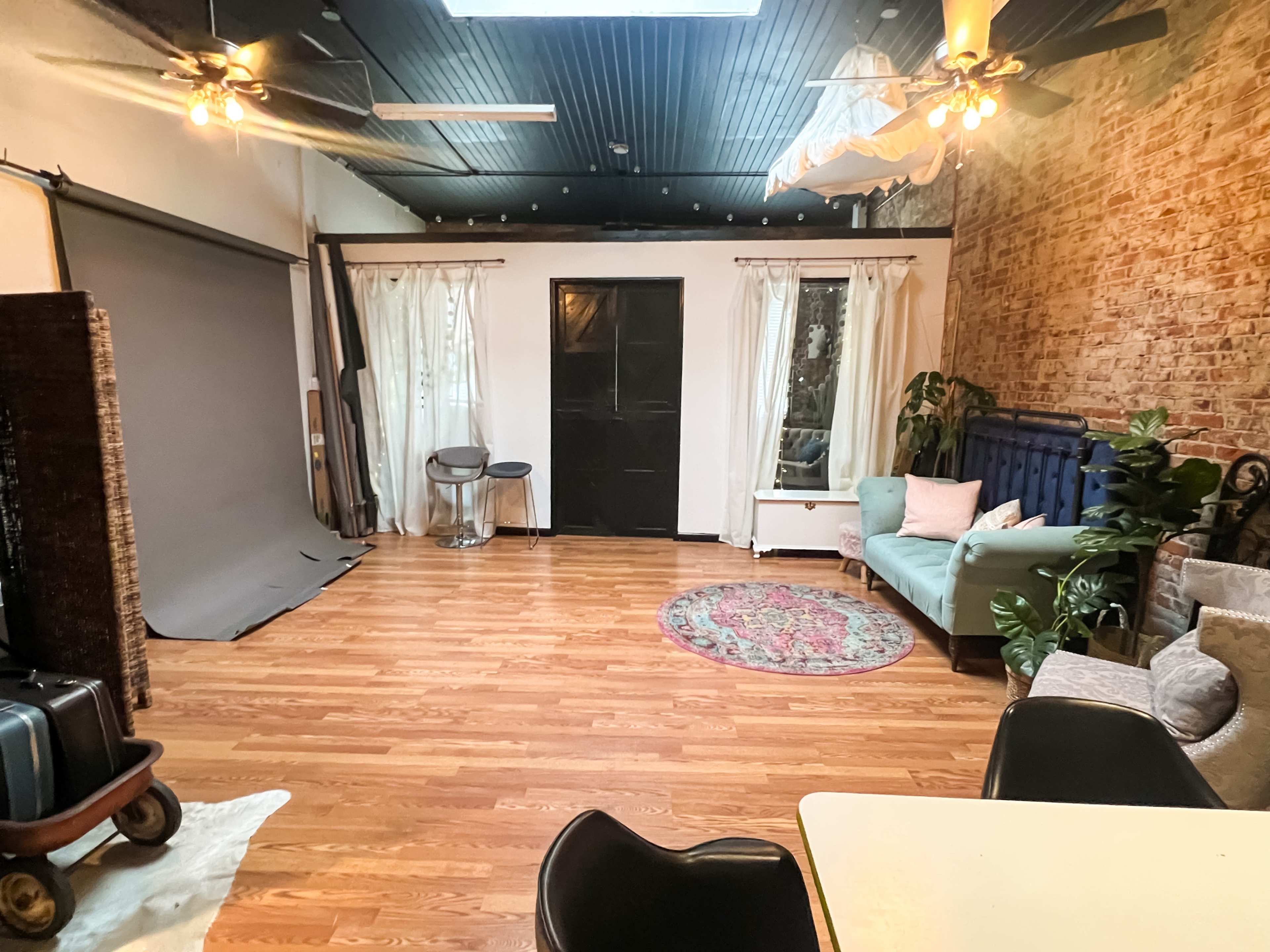 A spacious interior with hardwood floors, featuring a seating area with a blue couch, plants, a round rug, and a backdrop setup on one side.
