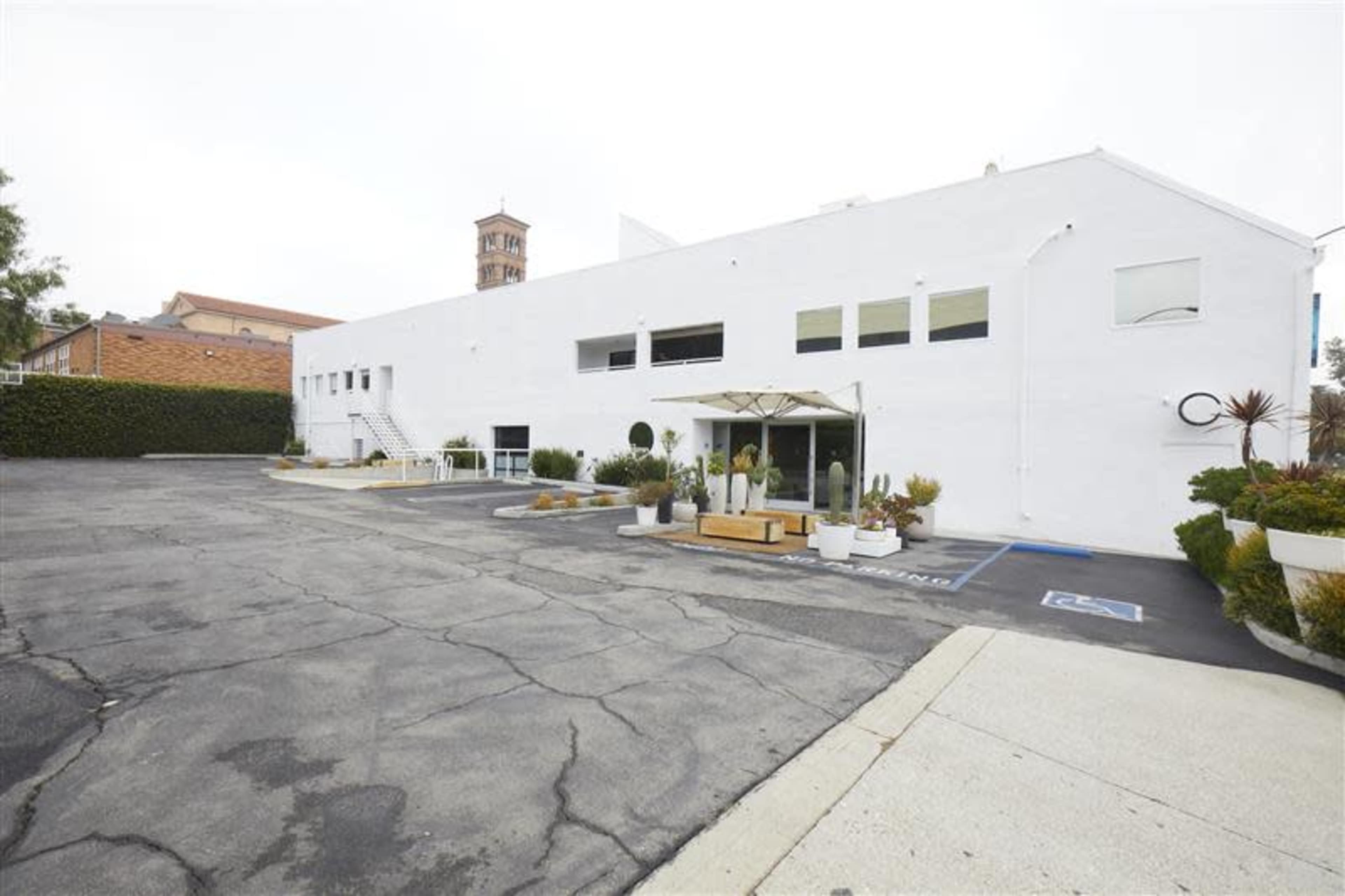 A white building with a parking lot and landscaped areas, located in an urban setting.