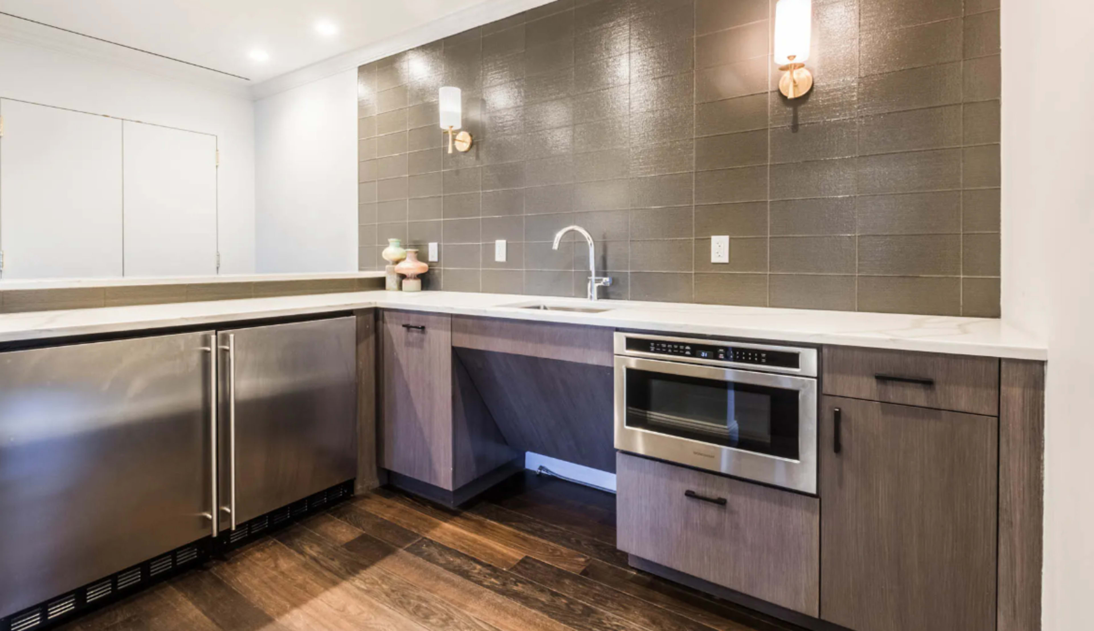 A modern kitchen with stainless steel appliances, a marble countertop, and a gray tiled backsplash.