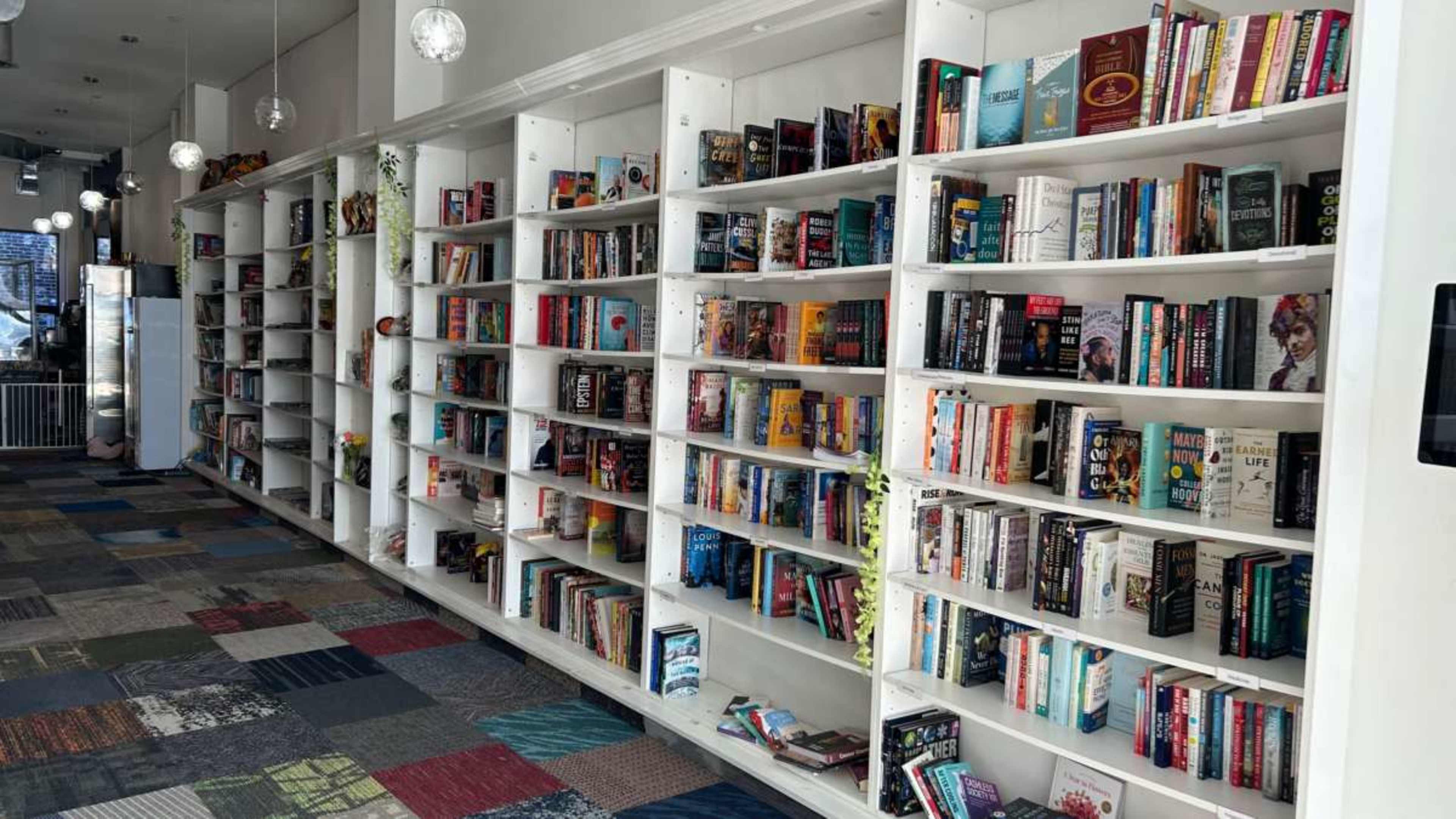 A series of white bookcases filled with various titles line the walls of a brightly lit room with a patterned carpet.