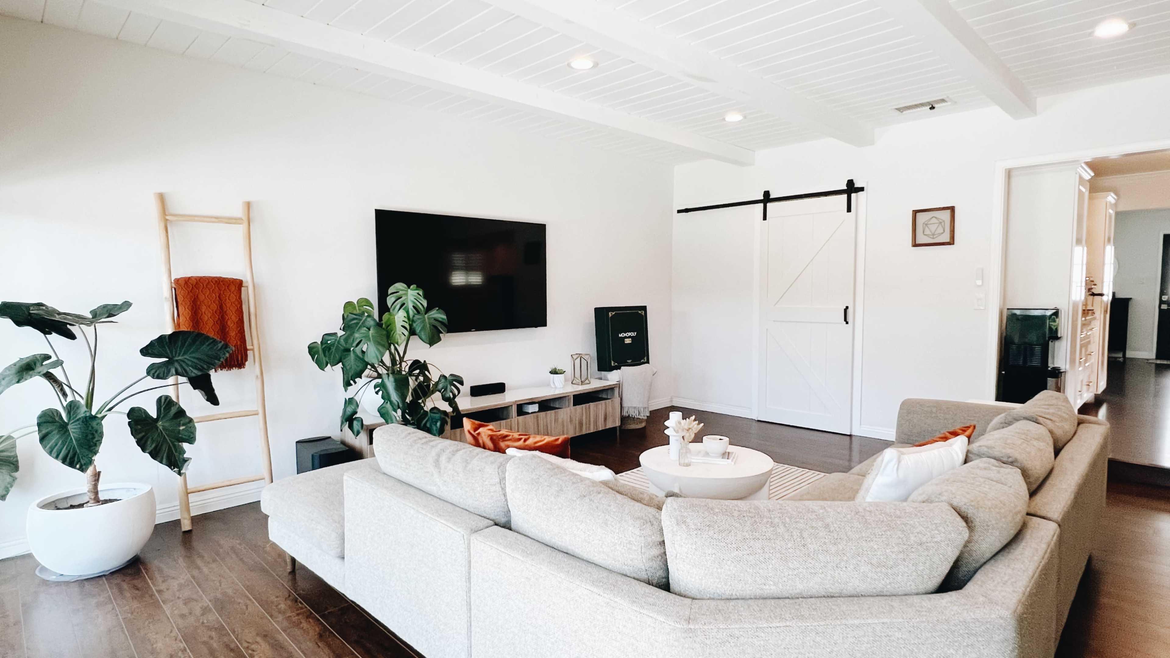 A modern living room features a large sectional sofa, a flat-screen TV mounted on the wall, and a sliding barn door leading to another room.