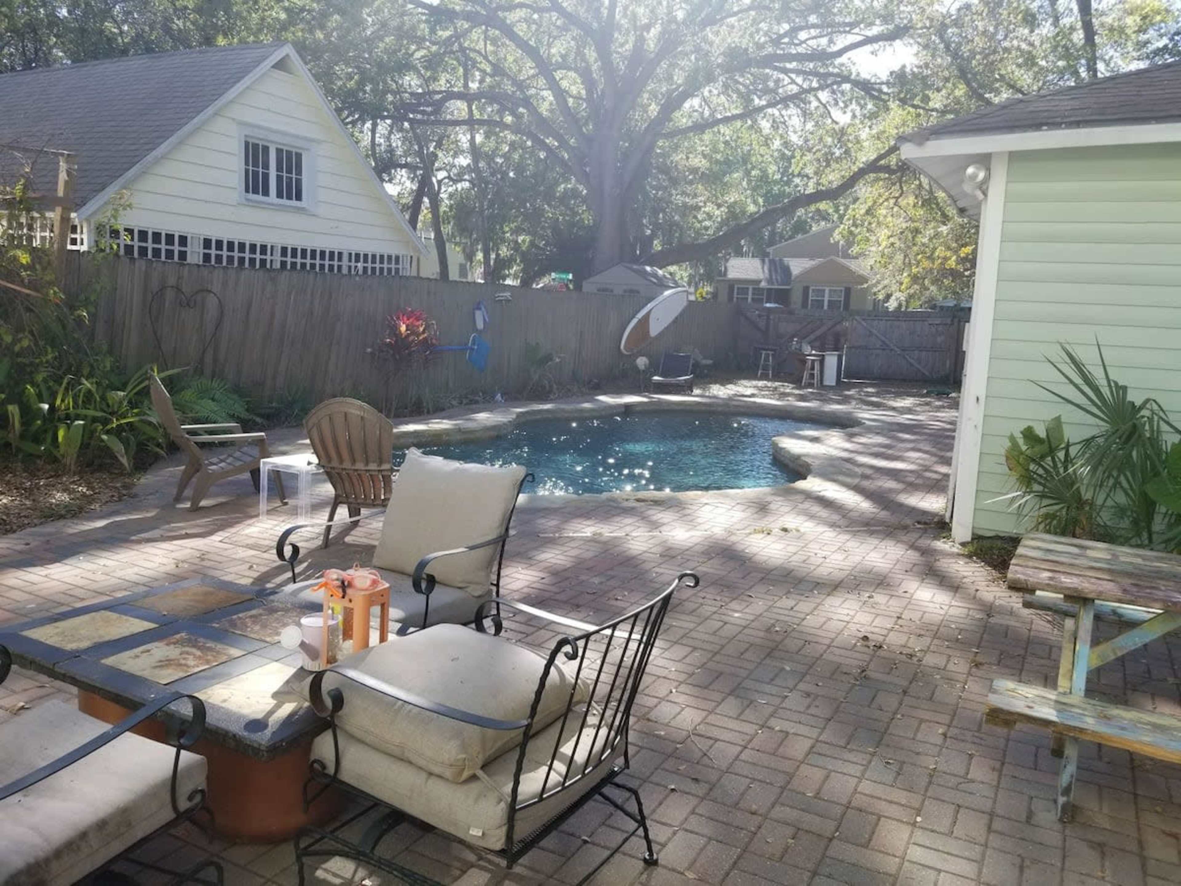 A backyard with a swimming pool surrounded by a patio, lounge chairs, and greenery.