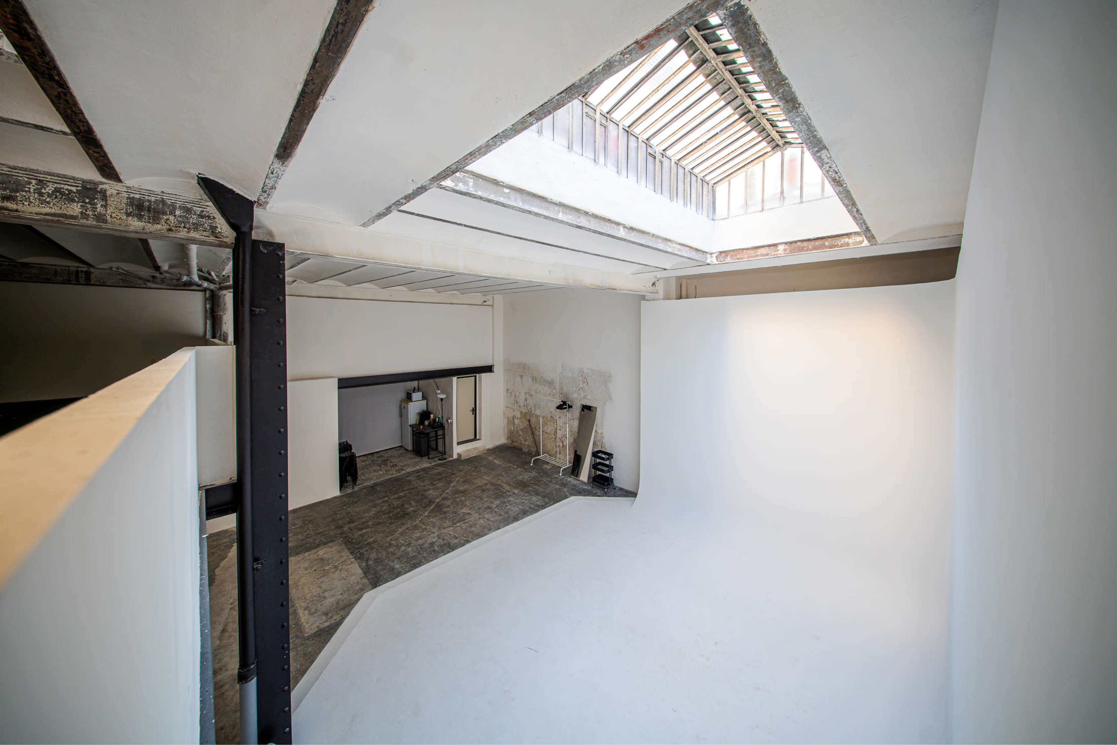 The image depicts a photography studio with a white backdrop, concrete flooring, and a skylight allowing natural light.