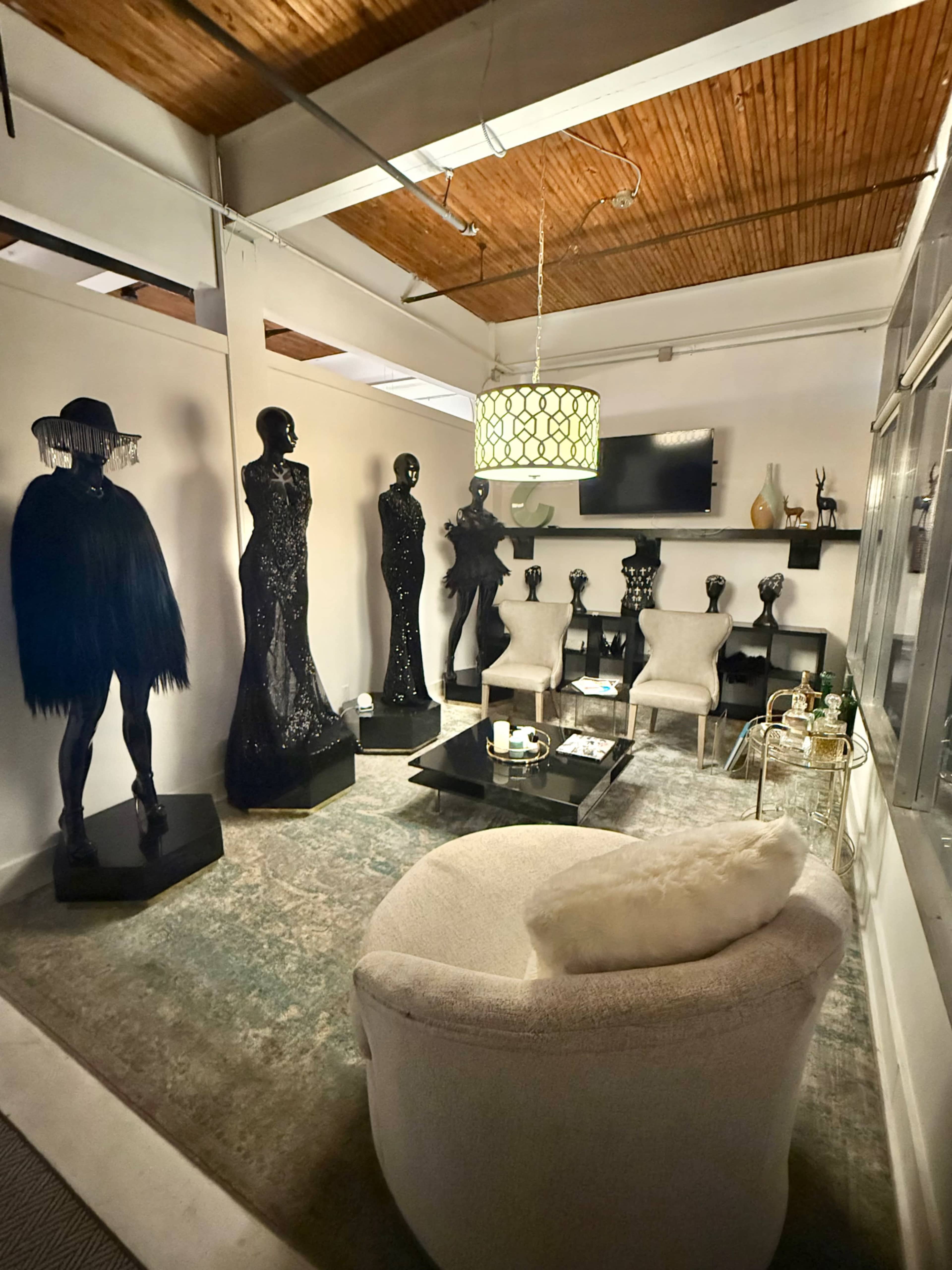 The image shows a stylish interior space featuring several black mannequin sculptures, two upholstered chairs, a circular coffee table, and a decorative light fixture.