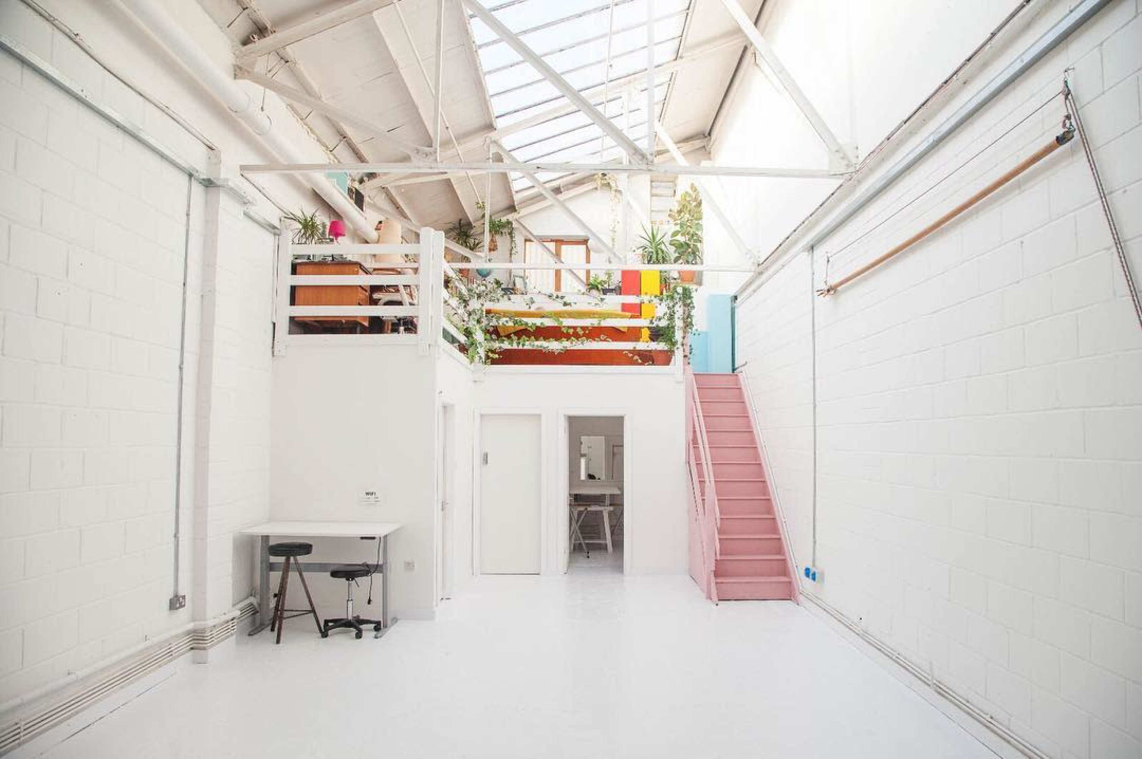 A bright, minimalist interior space with white walls, a staircase, and a loft area adorned with plants.